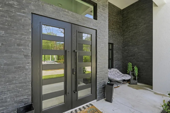 Double-door entry featuring glass panels and dark wood-finish framing, complemented by extensive dark stone-finish exterior cladding