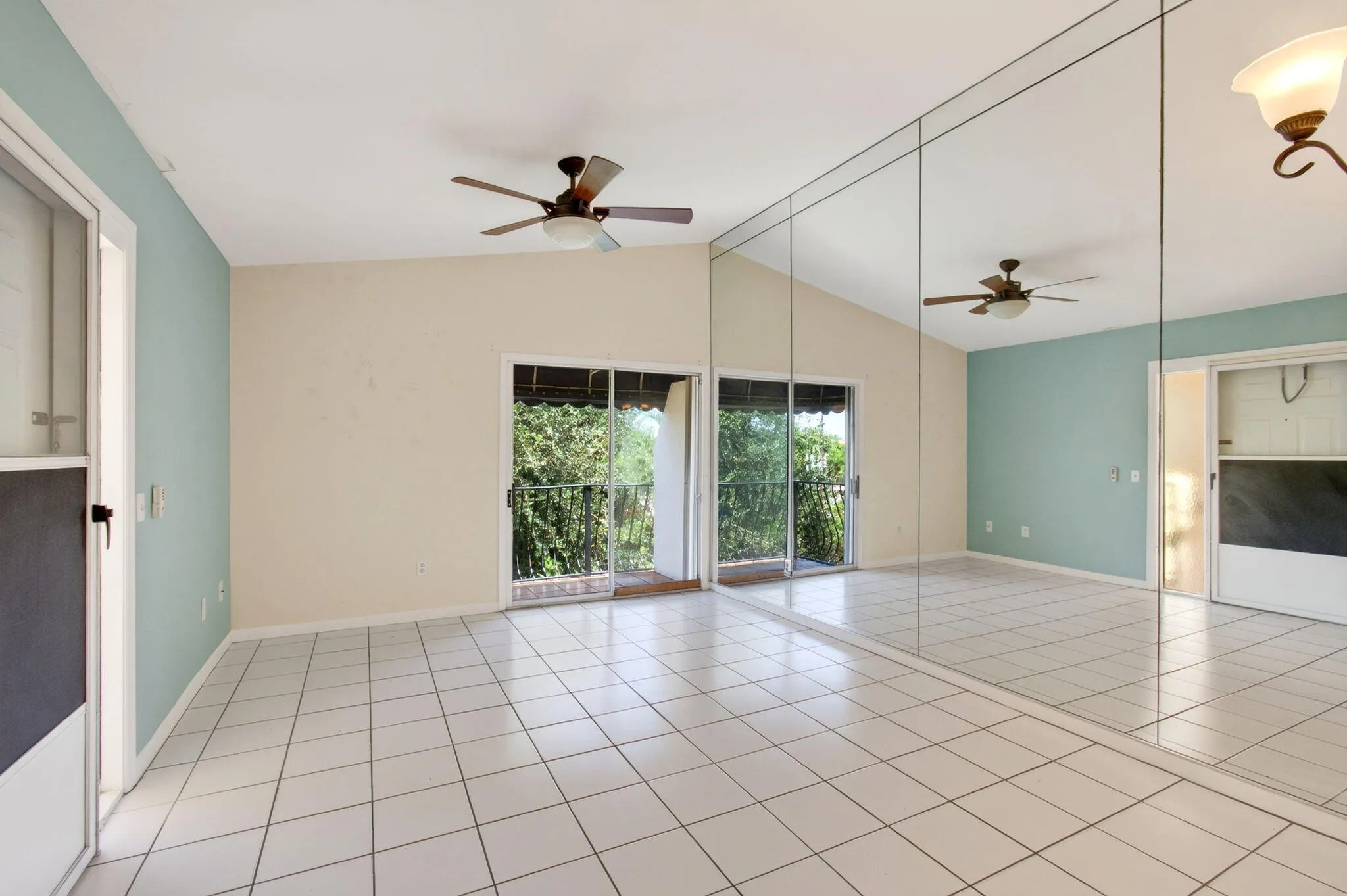 Vaulted ceiling, ceiling fan, full-wall mirrored accent, ceramic tile flooring, and sliding glass doors to a balcony