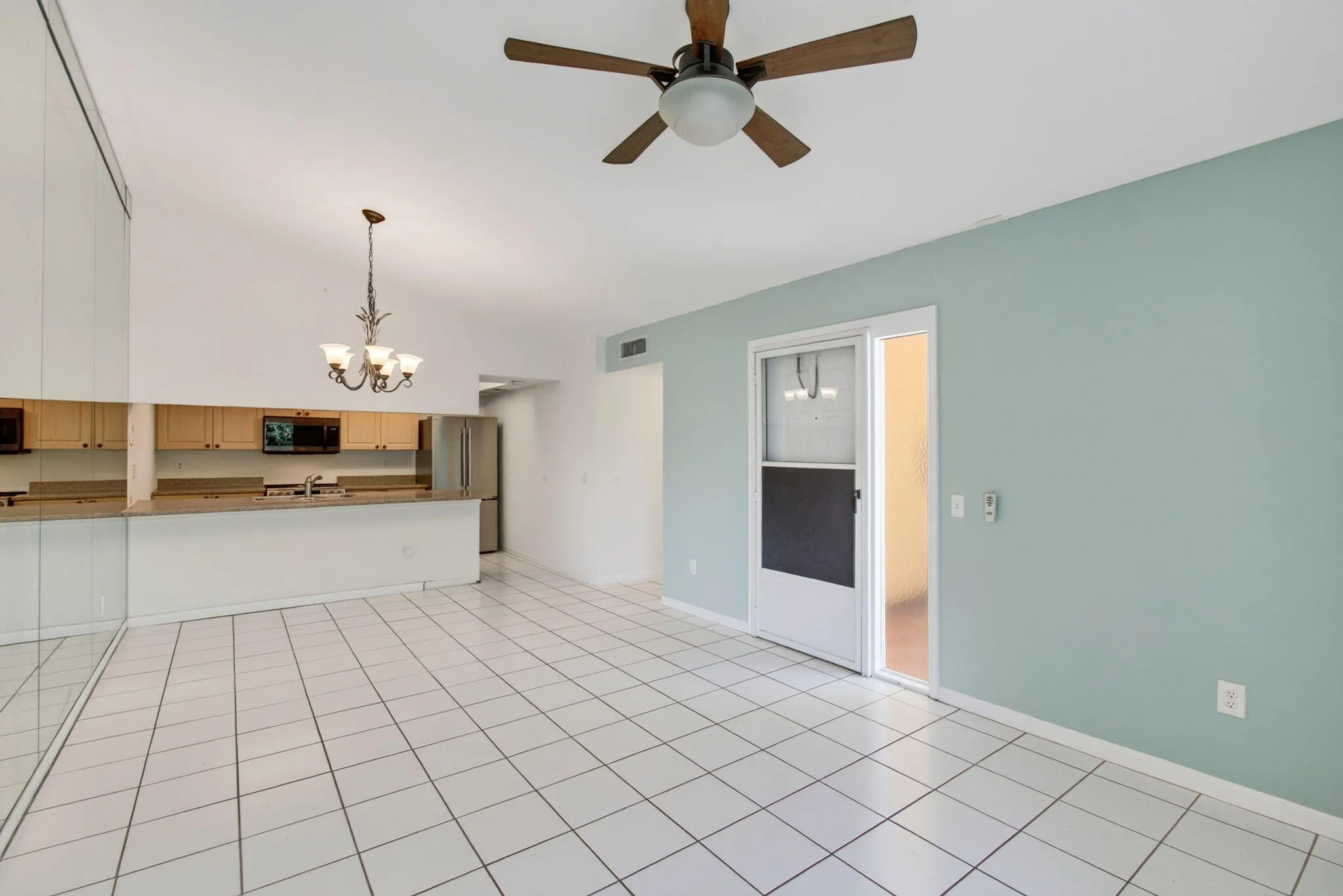 Vaulted ceiling with an attached ceiling fan, tile flooring, kitchen with light wood-finish cabinetry, built-in microwave, and stainless steel refrigerator