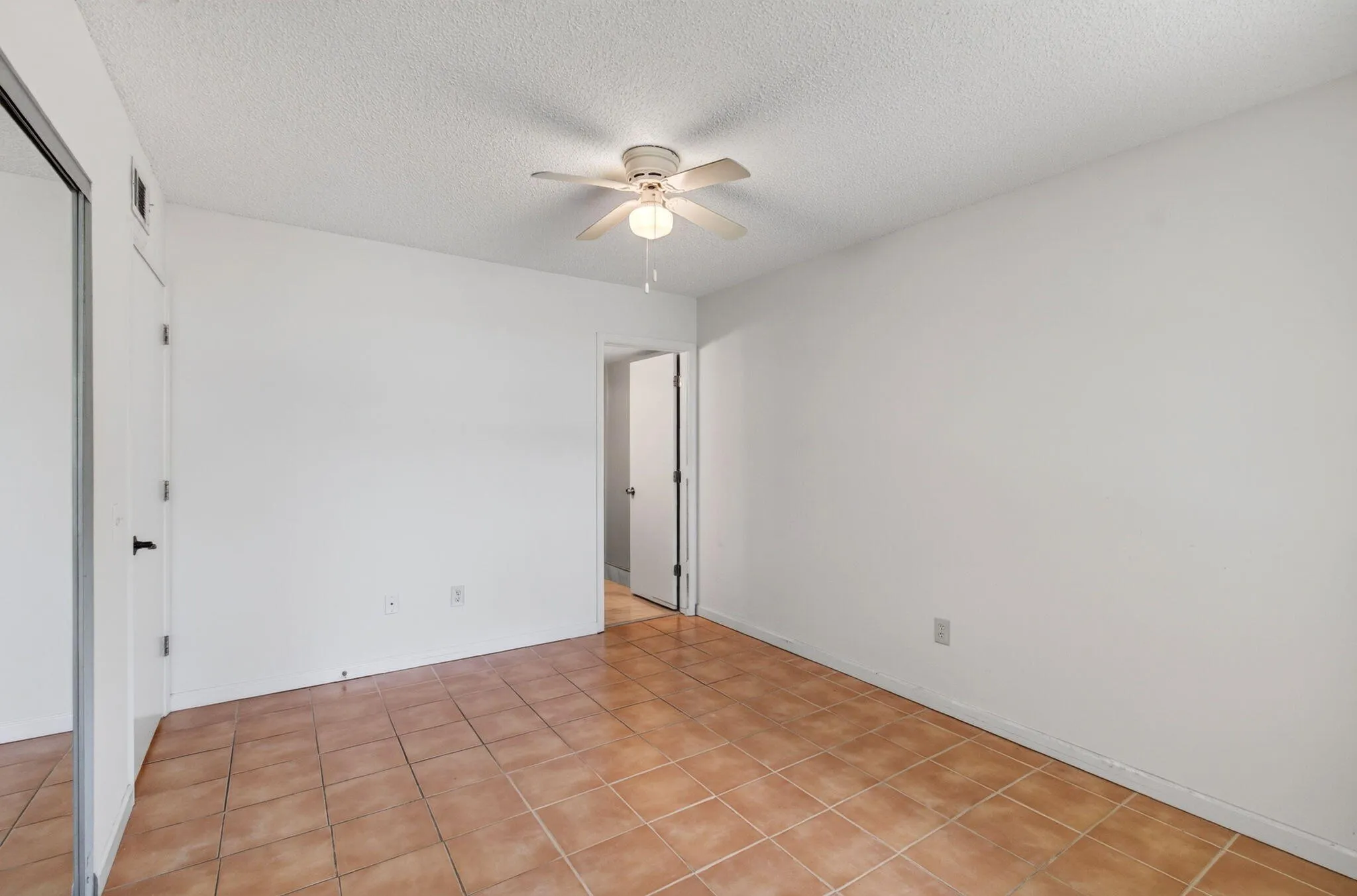 Neutral wall tones with a ceiling fan light fixture, tile flooring, and a mirrored closet door
