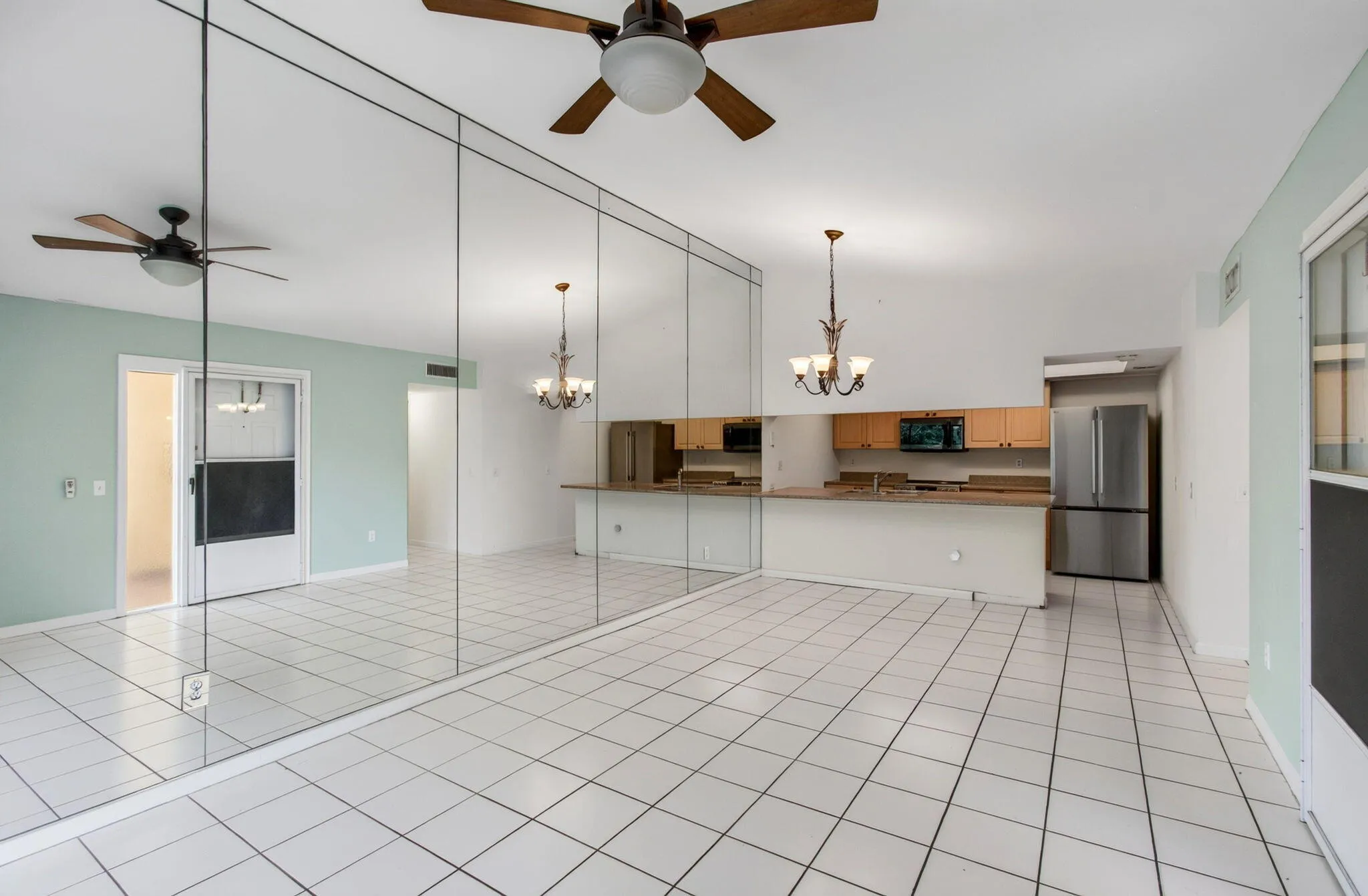 Open-concept living space with white tile flooring, mirrored wall, and vaulted ceilings