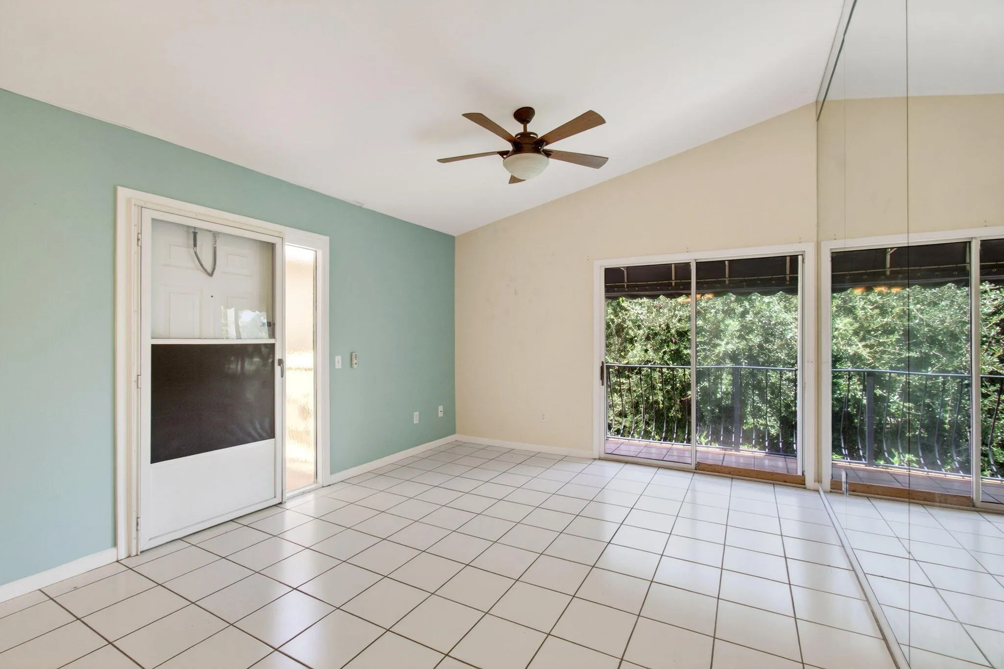 Vaulted ceilings, a ceiling fan, white tile flooring, and multiple sliding glass doors leading to an outdoor balcony