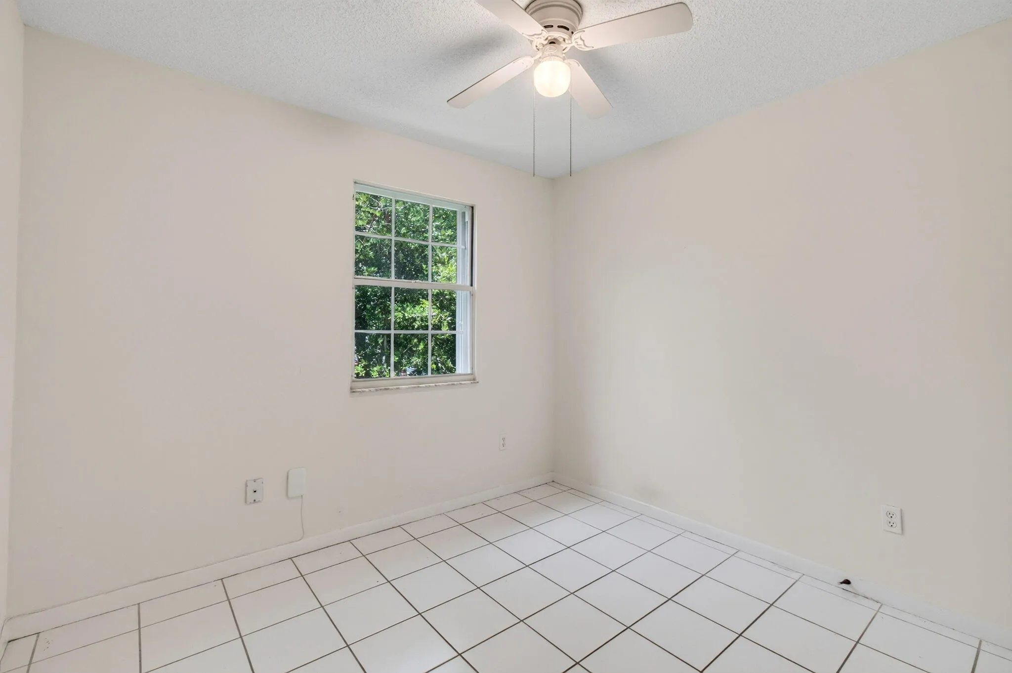 Room featuring white tile flooring, a single window, and a ceiling fan with light fixture