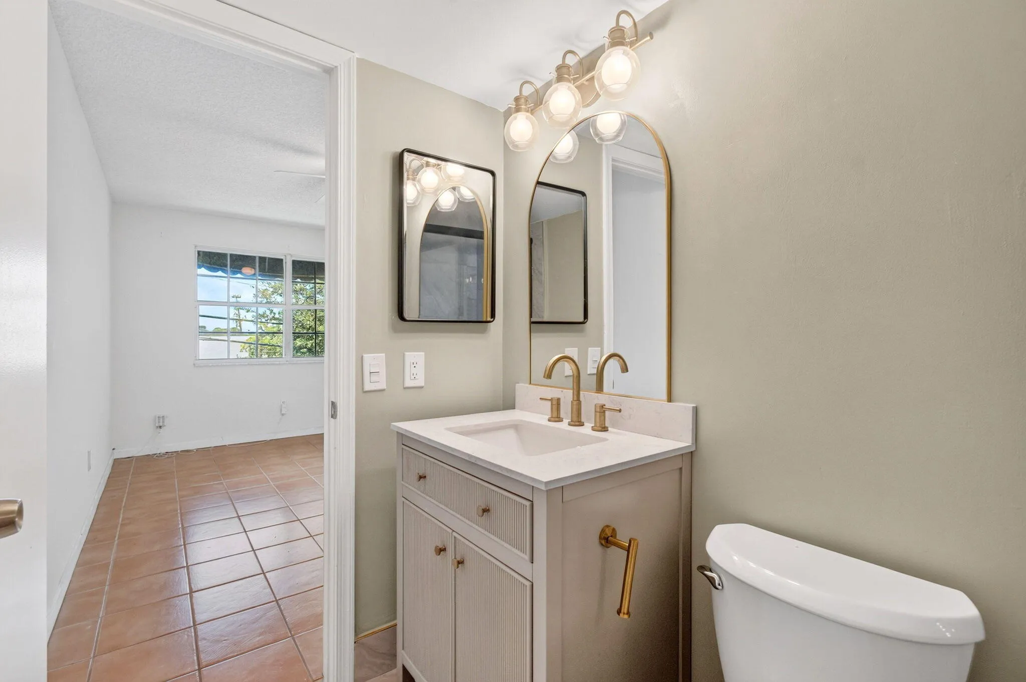 Bathroom vanity with integrated sink, gold-finish fixtures, and arched mirror