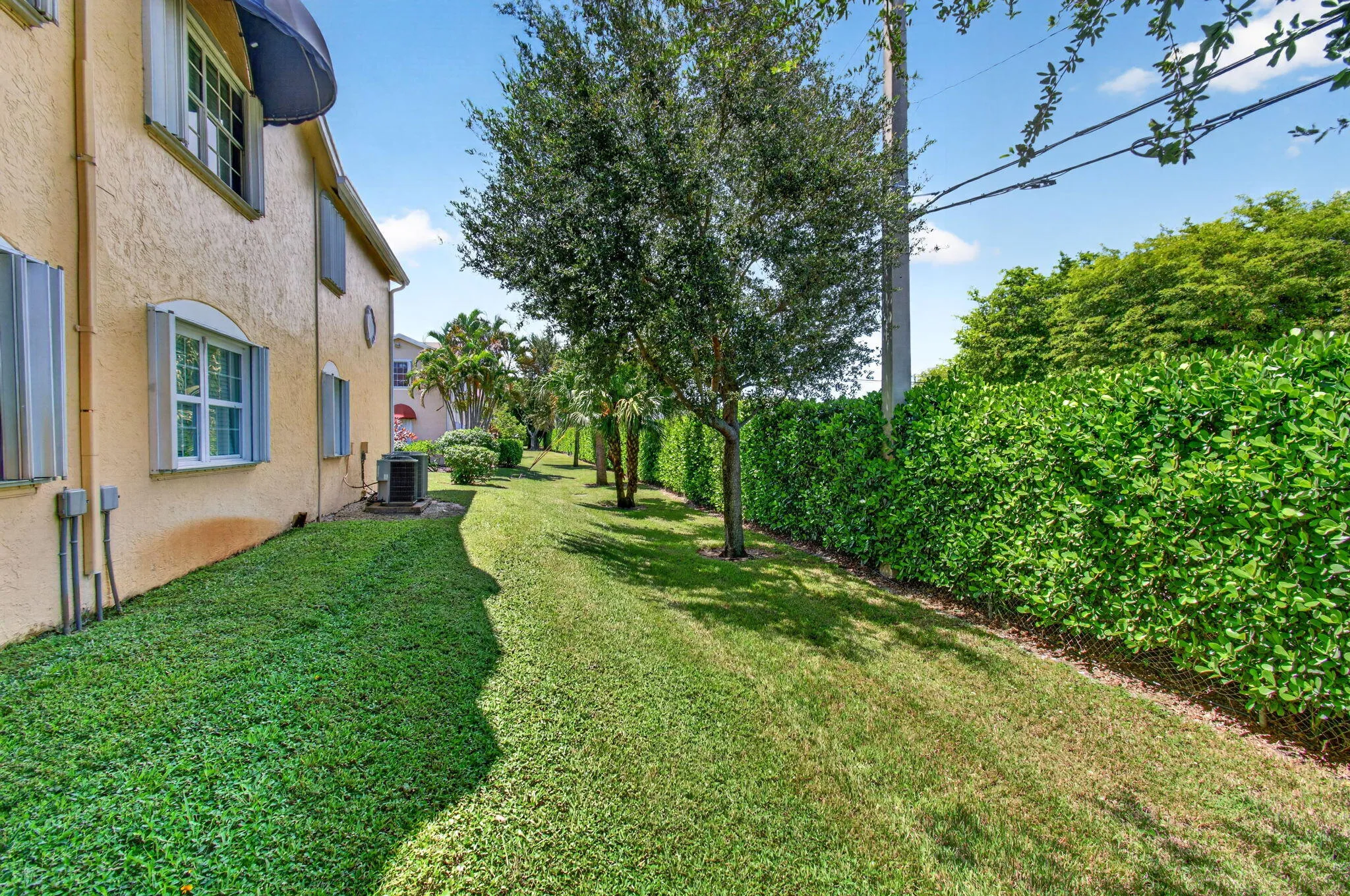 Stucco exterior with multiple windows, mature trees, and a lush green lawn