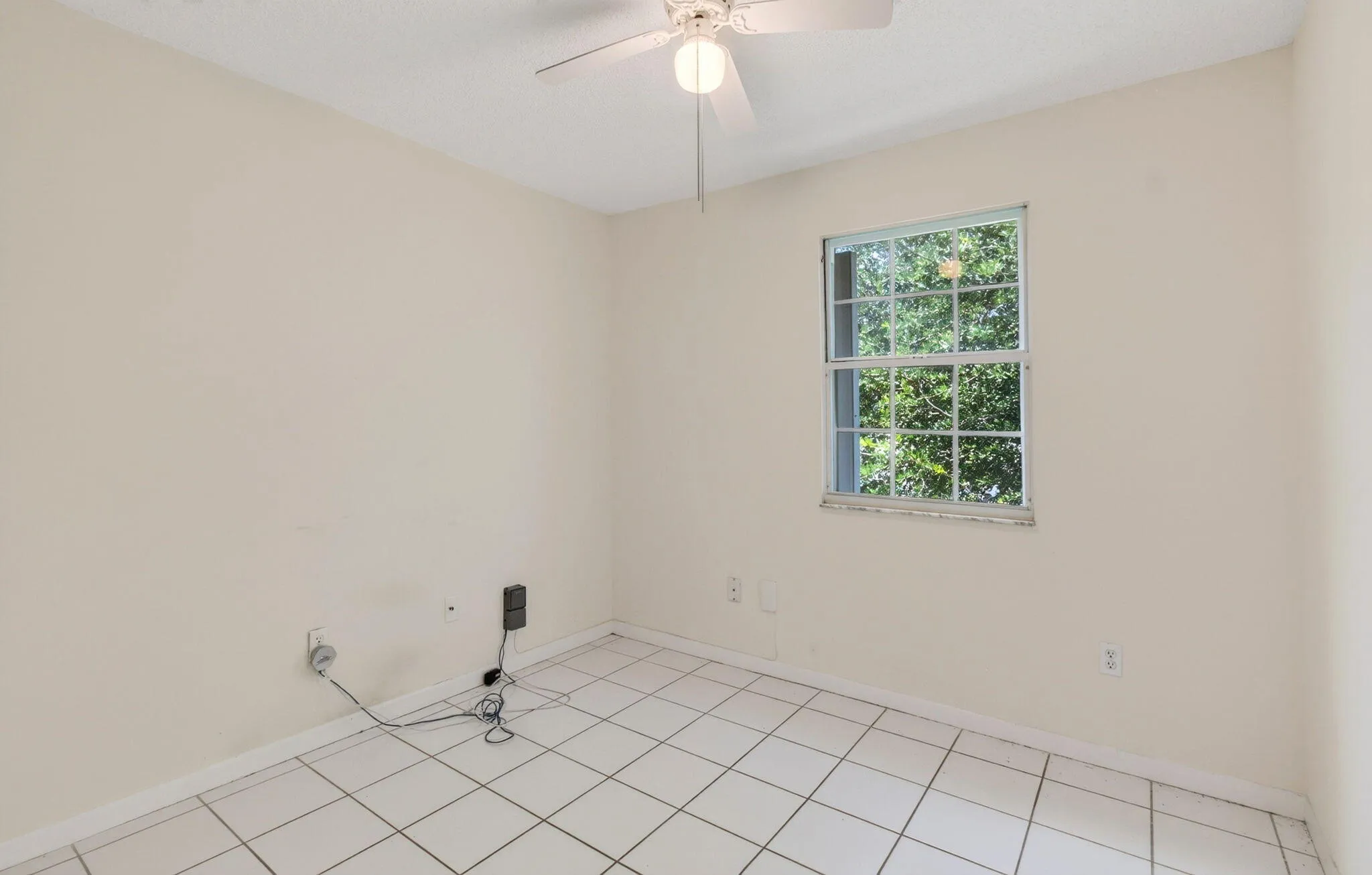 White tile flooring, a window with exterior tree scenery, and a ceiling fan with integrated lighting