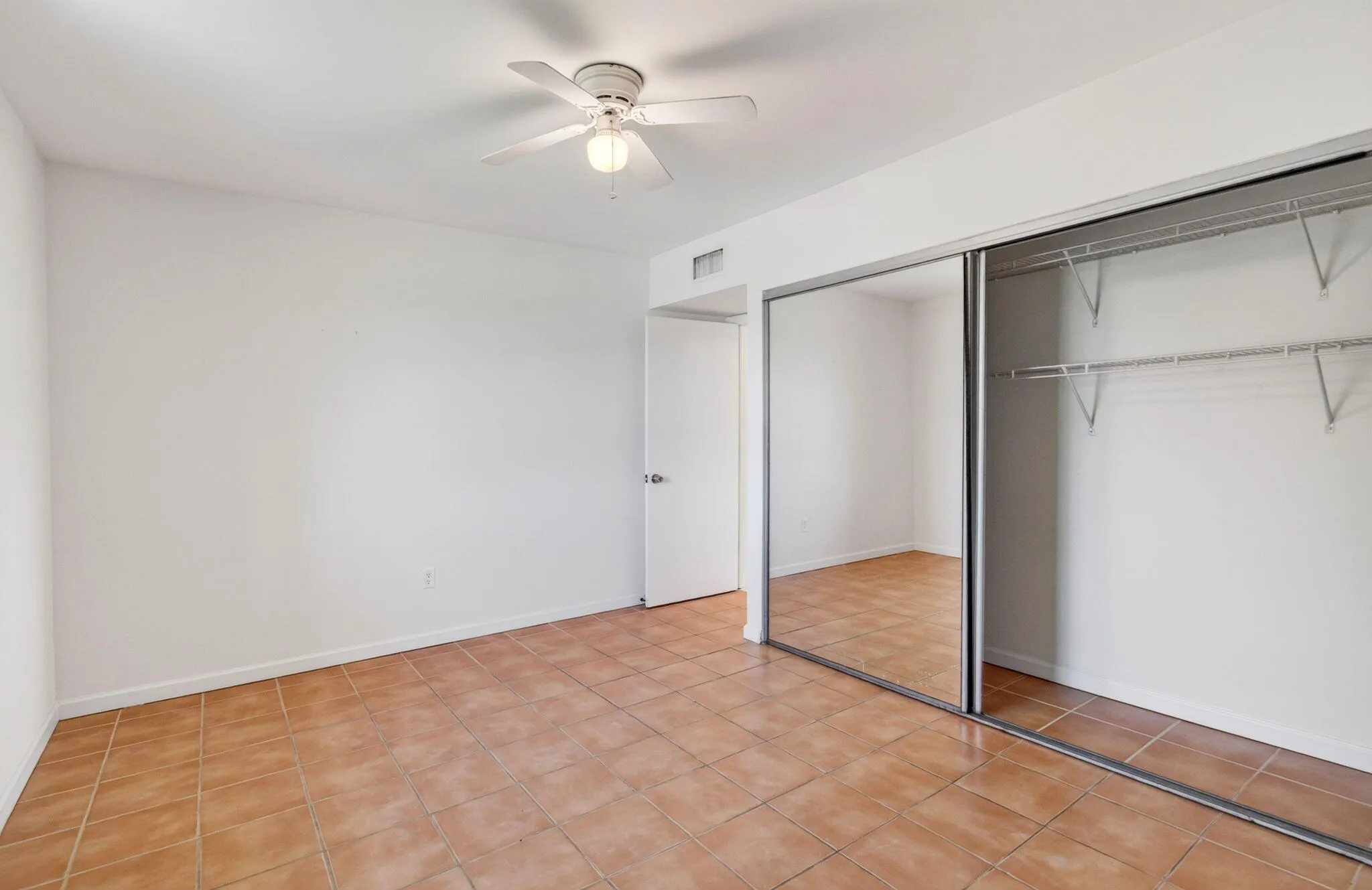 Ceramic tile flooring throughout, ceiling fan, mirrored closet doors, and wire shelving