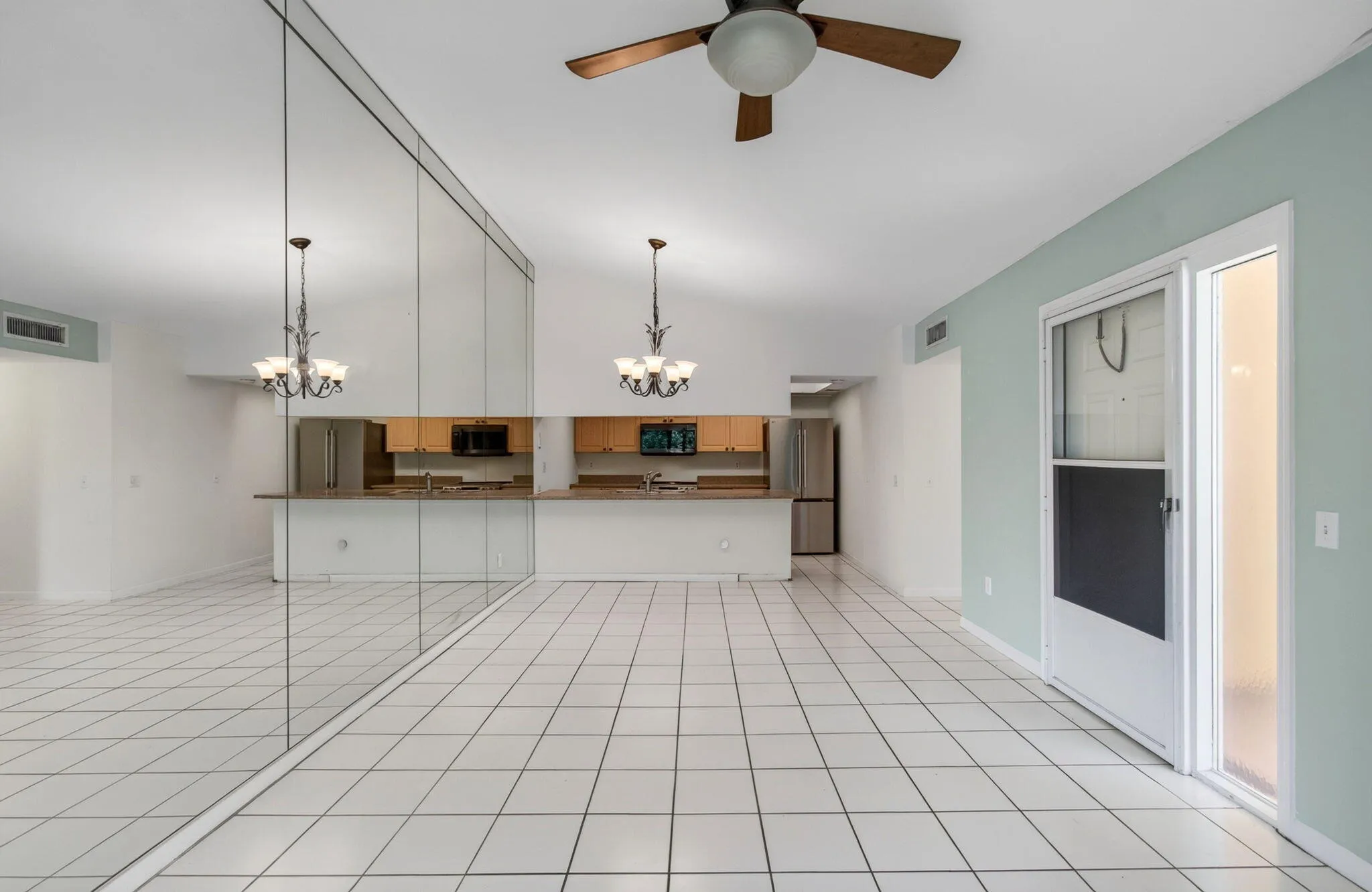 Vaulted ceilings, white tile flooring, ceiling fan, mirrored wall paneling, and sliding glass doors