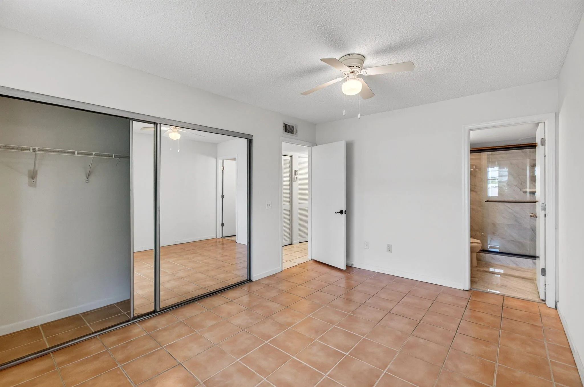 Tile flooring, mirrored closet doors, ceiling fan with integrated lighting, and an adjacent bathroom with a tiled shower enclosure