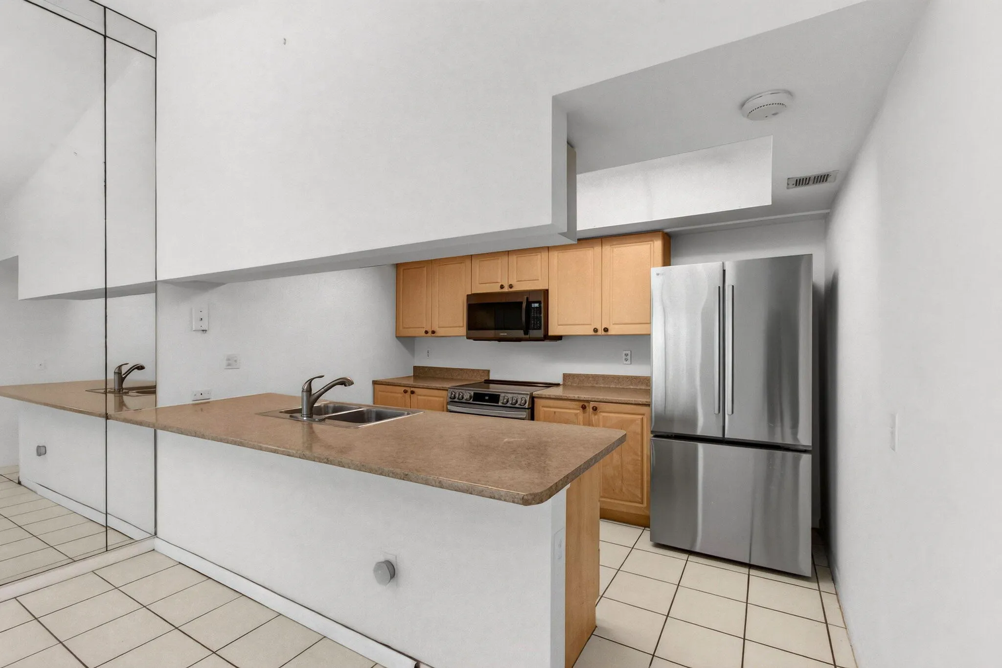 Kitchen featuring stainless steel appliances, wood cabinetry, stone countertops, and tile flooring