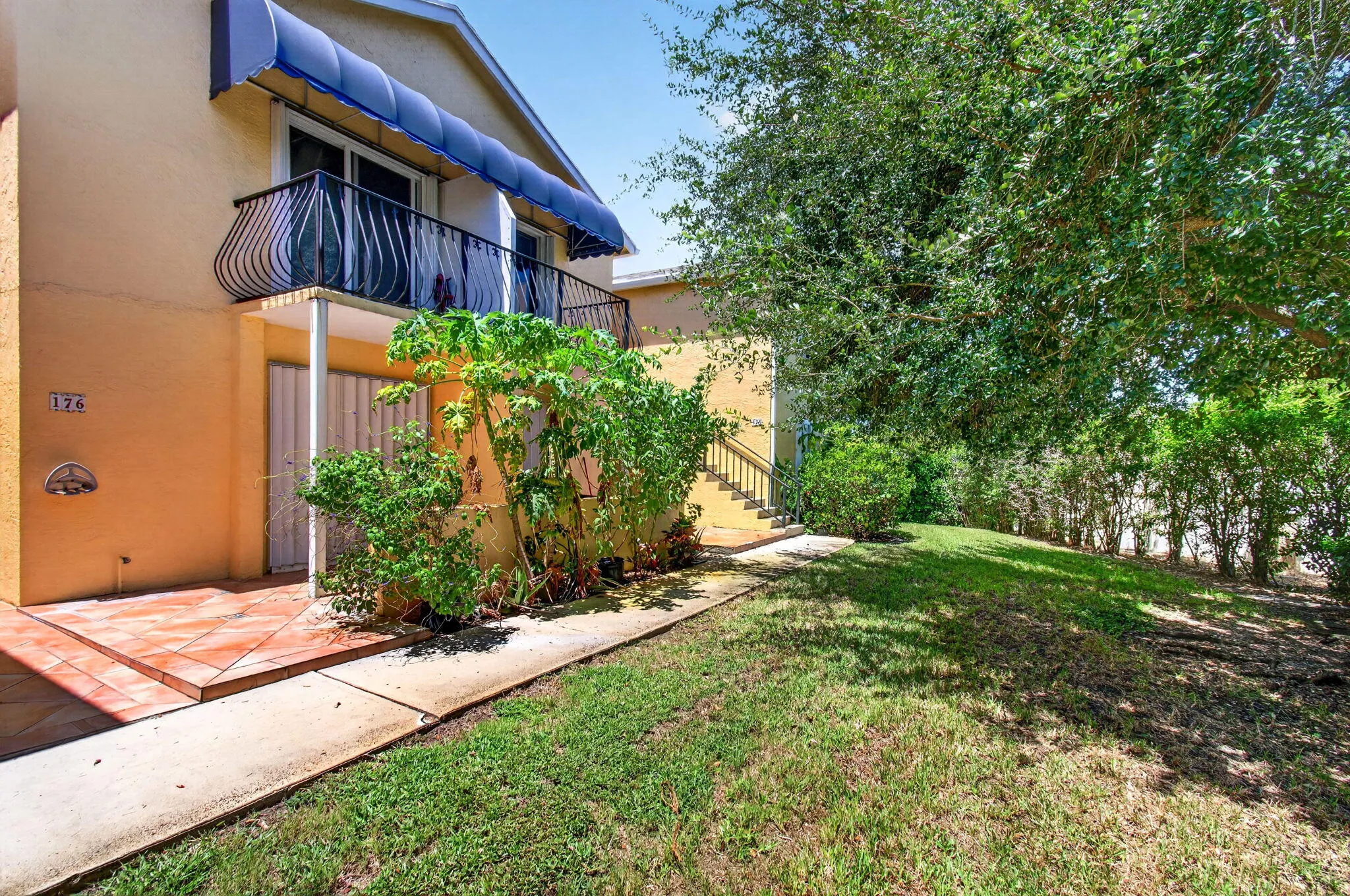 Charming residence featuring a striped awning, terra cotta tile entry, and an expansive lawn with mature trees providing natural landscaping