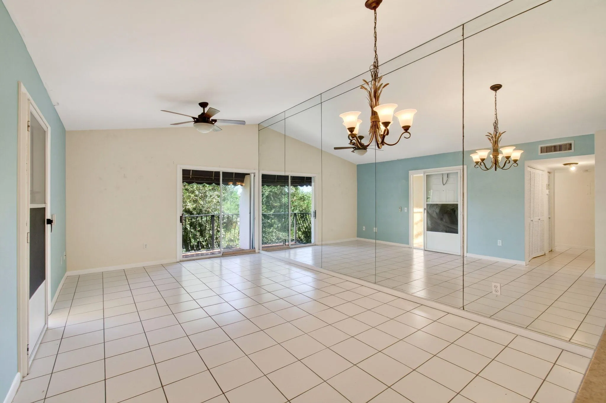 Vaulted ceiling with a ceiling fan, full wall of mirrors, sliding glass doors, white tiled flooring, and a multi-arm chandelier