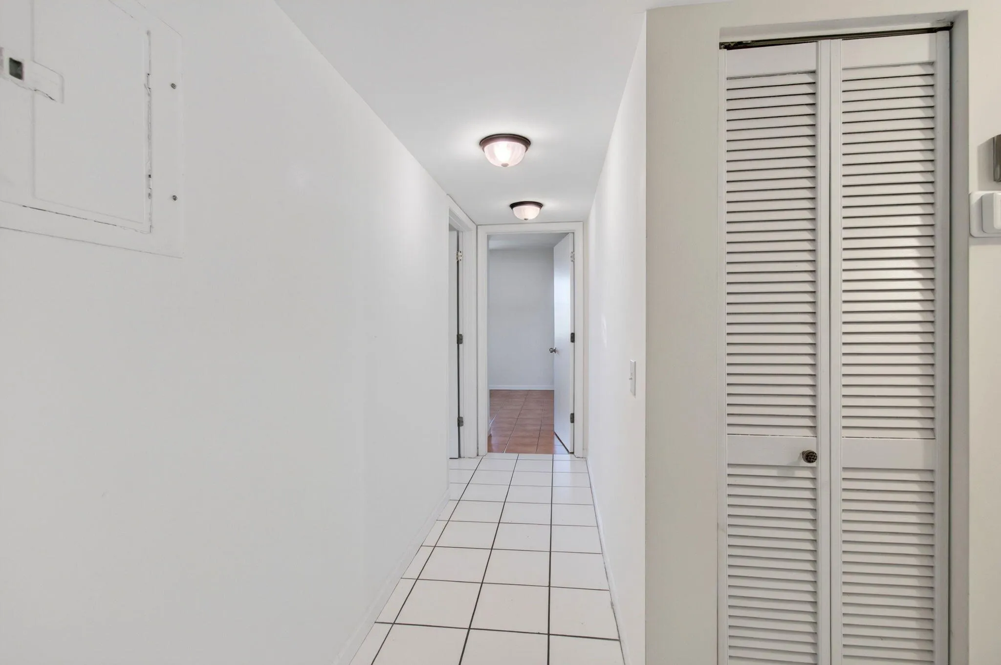 Hallway featuring square tile flooring, flush mount lighting fixtures, and louvered bi-fold doors