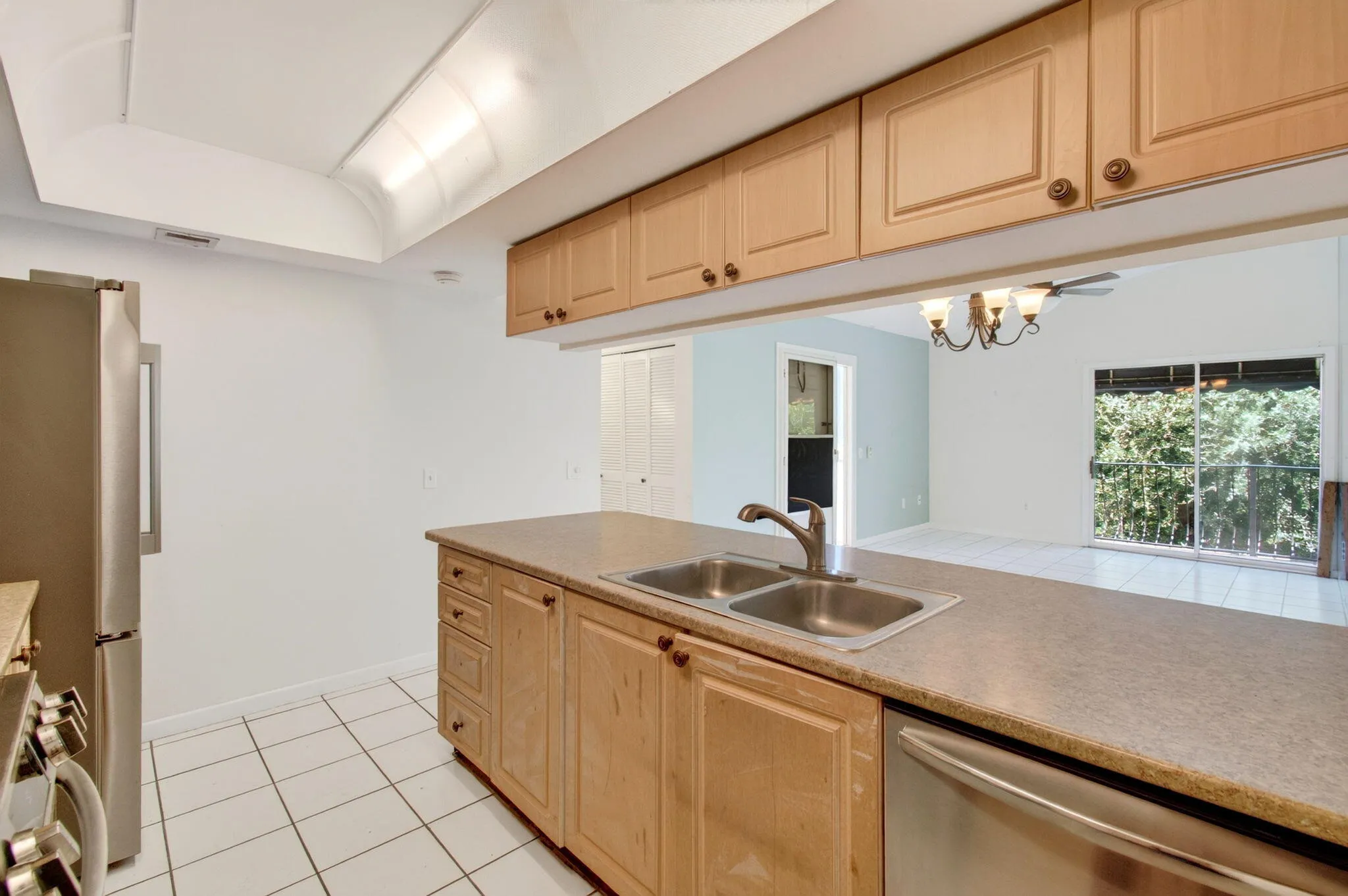 Kitchen featuring a stainless steel double sink, light wood cabinetry, white tile flooring, and a stainless steel refrigerator