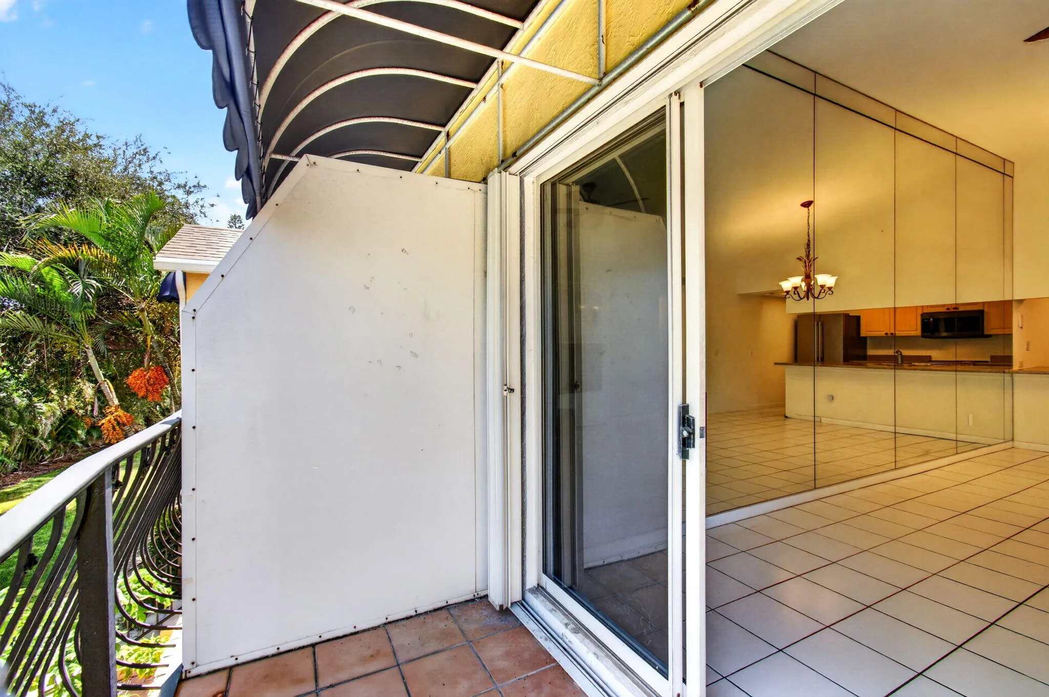 Terracotta tile balcony with wrought iron railing, awning, and sliding glass door