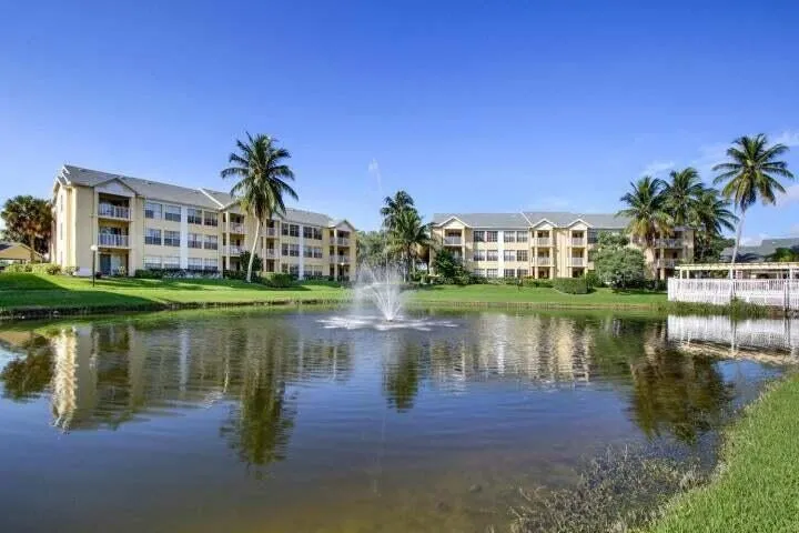 Residences featuring private balconies, situated on a landscaped property with a tranquil pond, fountain, and palm trees