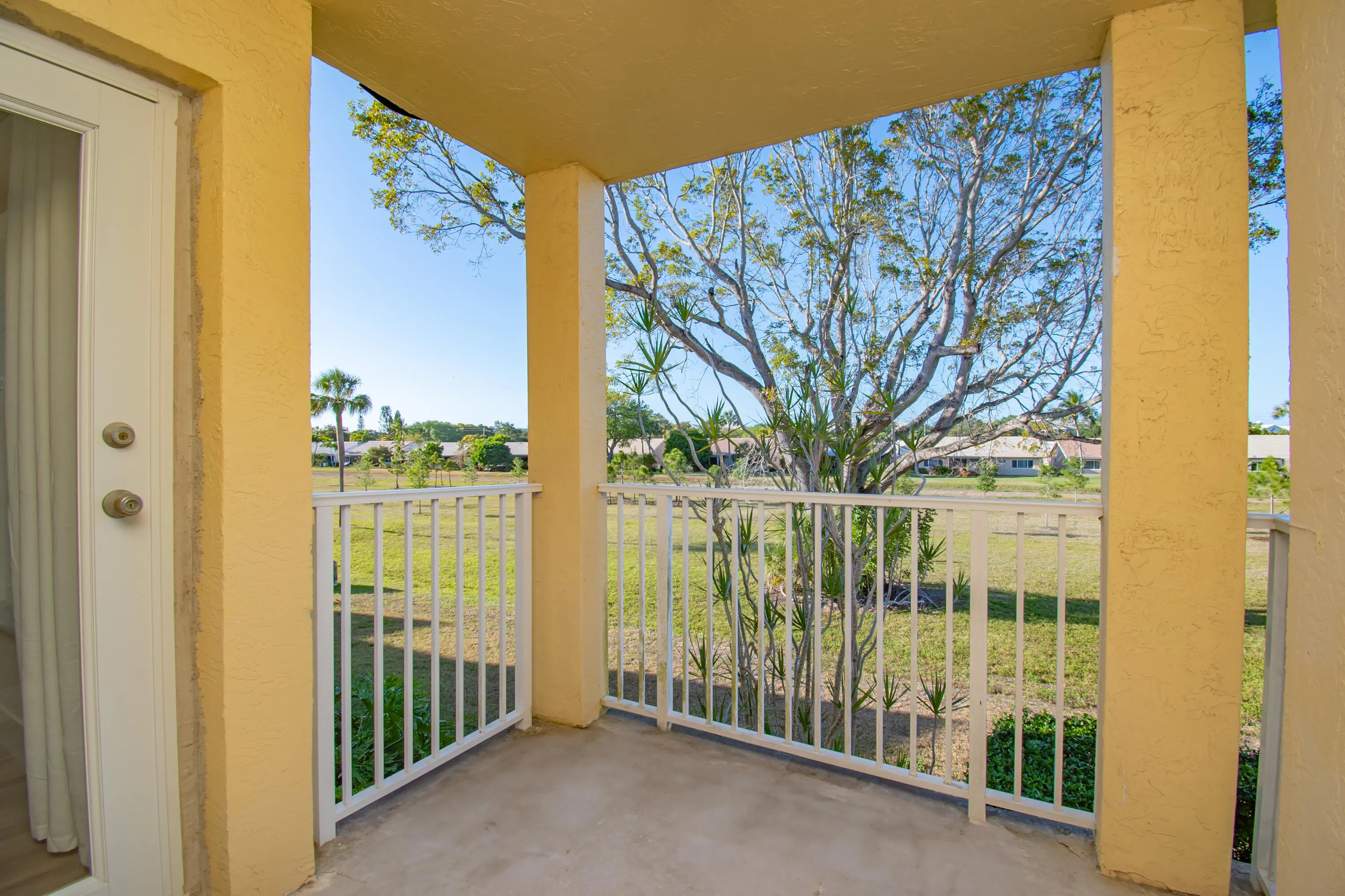 Covered patio with a view and privacy. Textured walls, concrete flooring, and white railings
