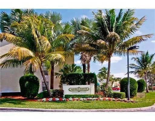 Manicured landscaping with diverse palm trees, an illuminated community sign, and a paved curb