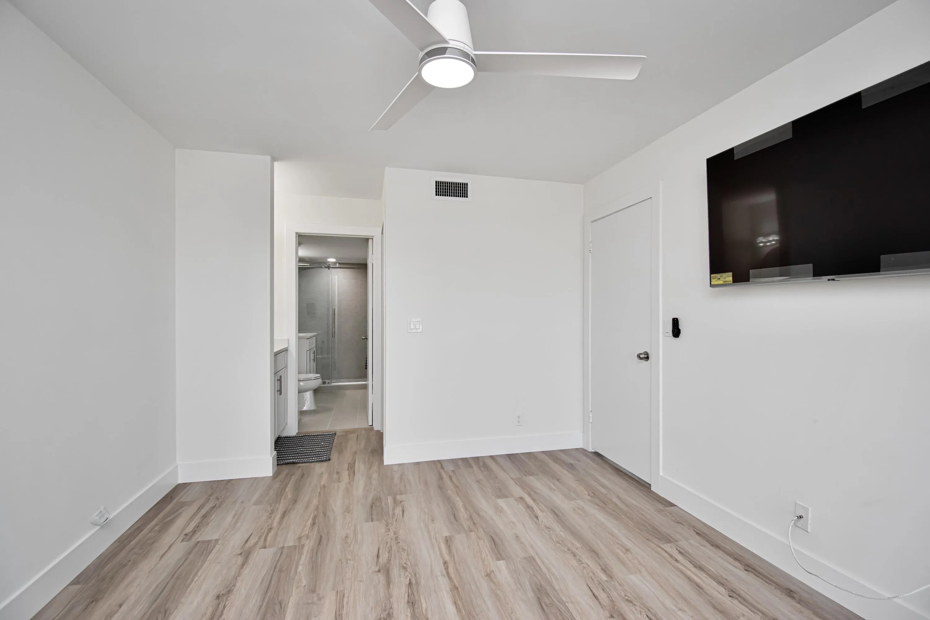 Wood-finish flooring, ceiling fan with integrated lighting, and a neutral white wall palette