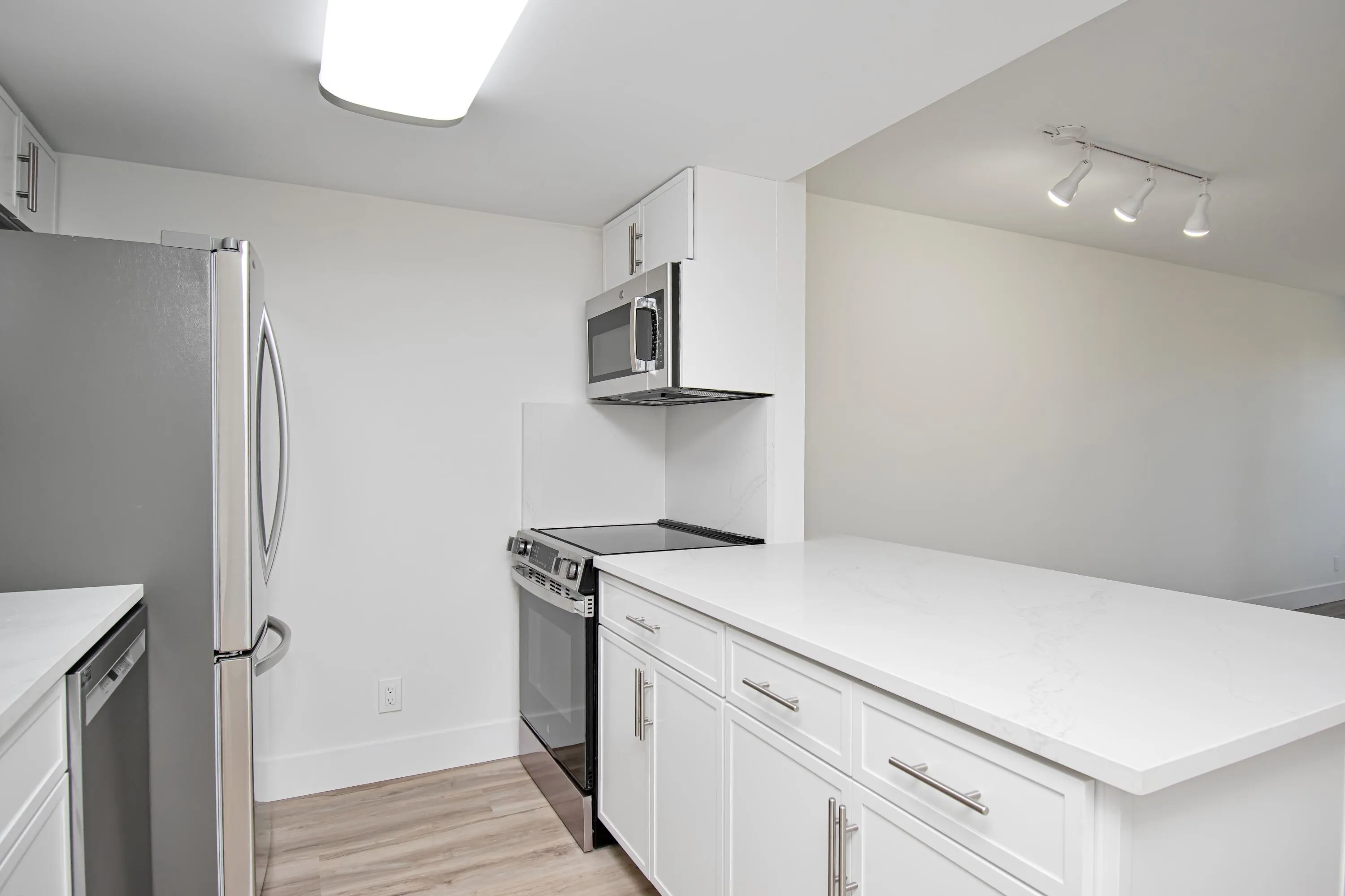 Stainless steel appliances, white cabinetry, integrated microwave, wood-finish flooring, and a large countertop space