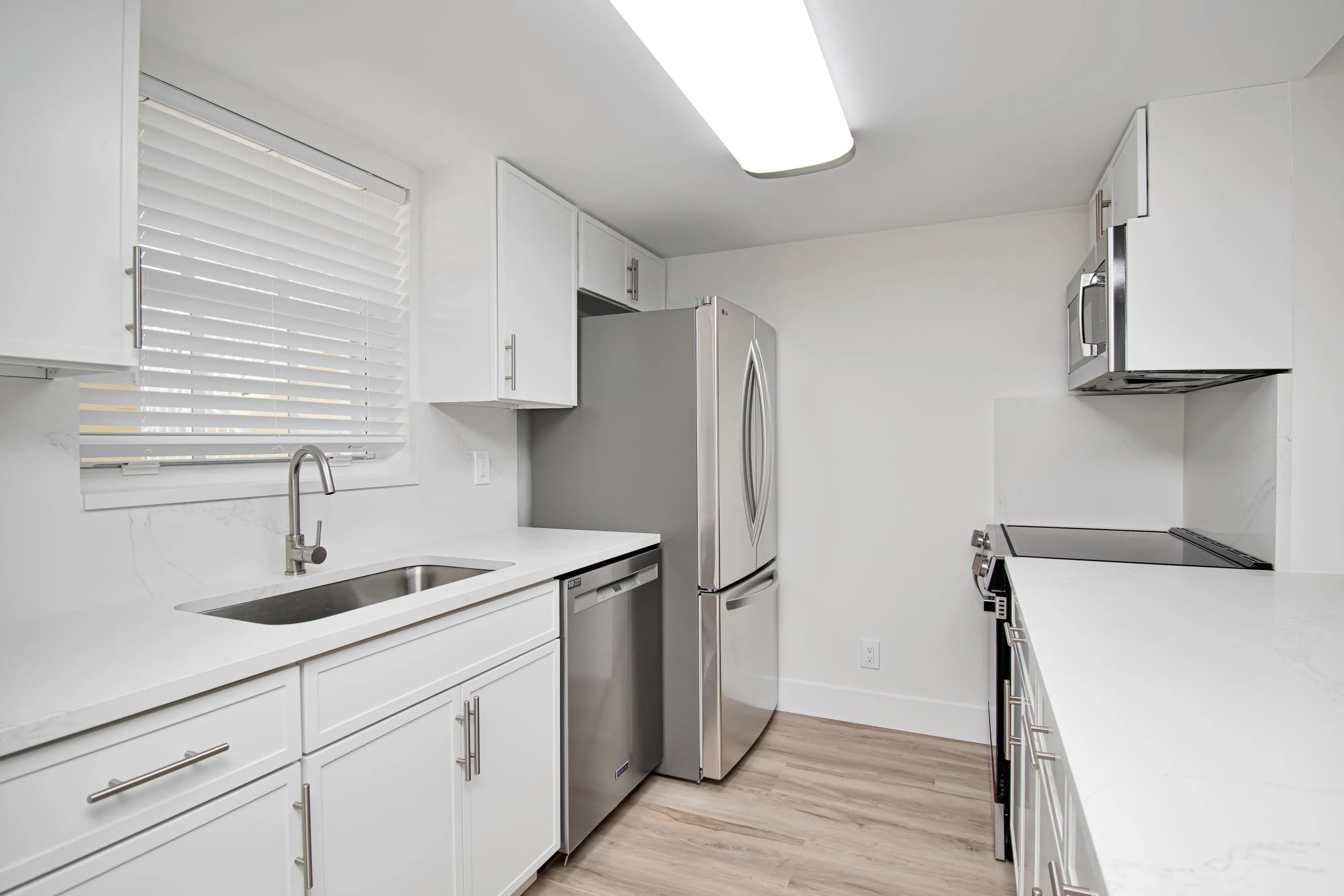 White cabinetry with brushed nickel hardware, stainless steel appliances, light-toned wood-finish flooring, and solid surface countertops