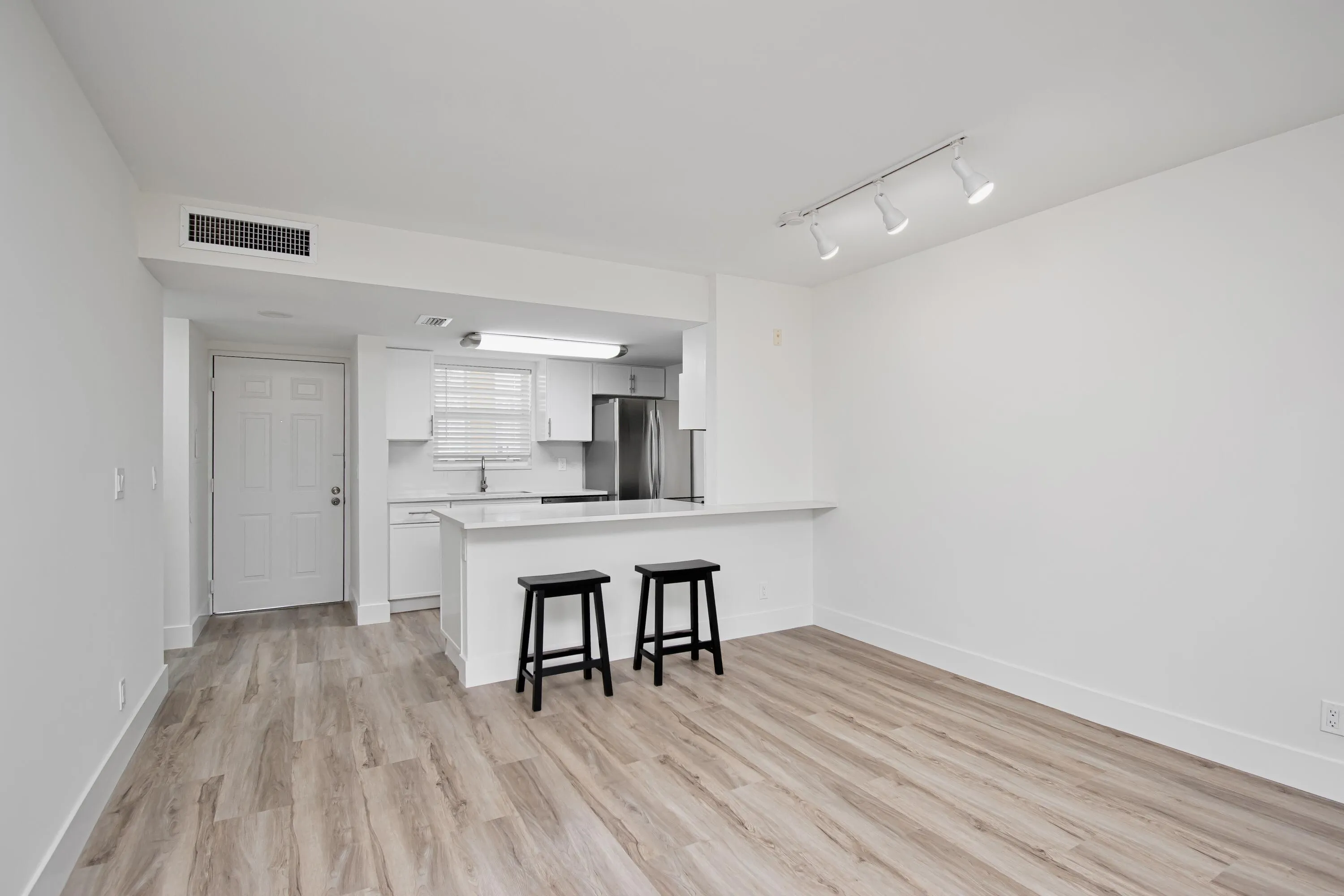 Wood-finish flooring, white kitchen cabinetry, stainless steel appliances, white countertops, and track lighting fixtures
