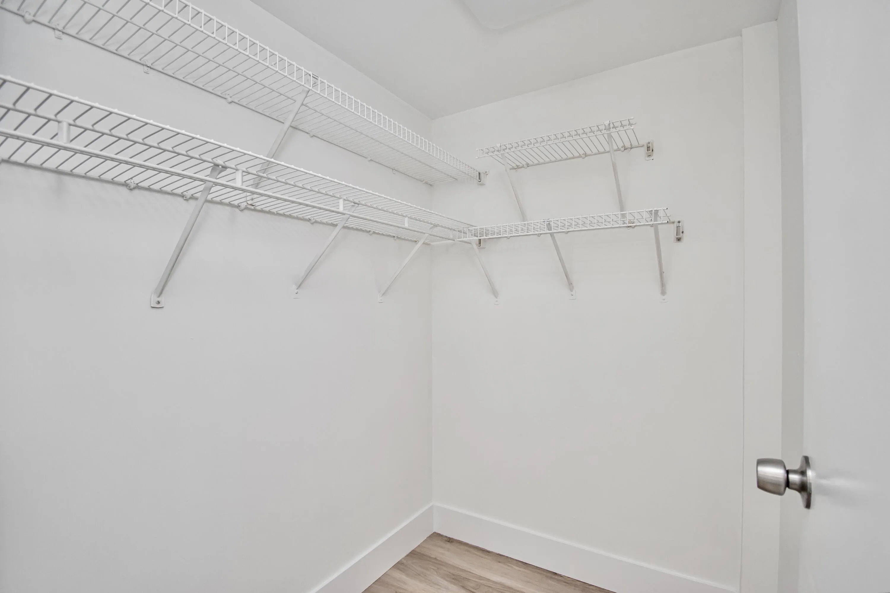 Walk-in closet with white wire shelving and wood-finish flooring