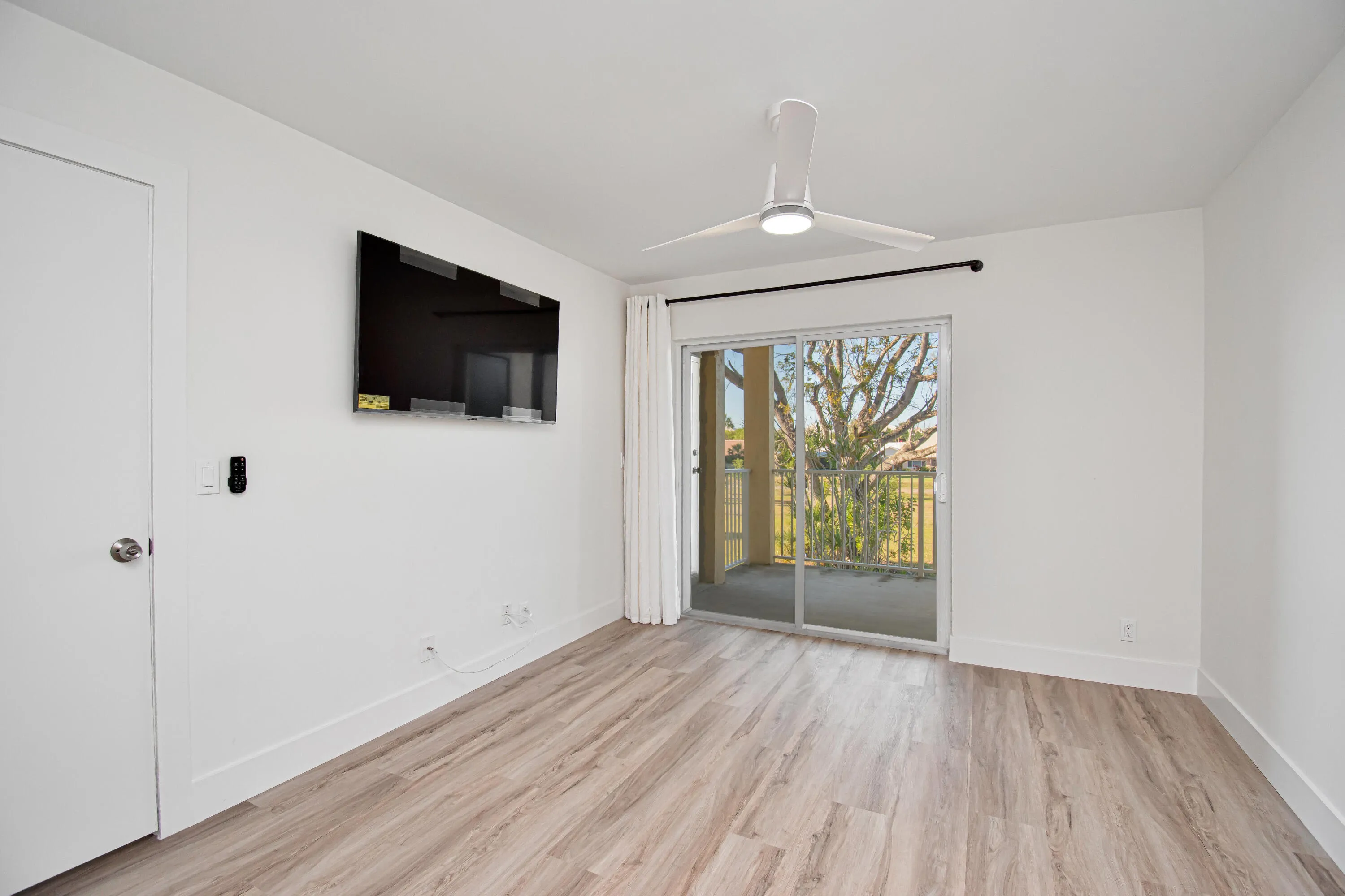 Light wood-finish flooring, 55" UHD TV, white walls, and a modern ceiling fan with integrated lighting