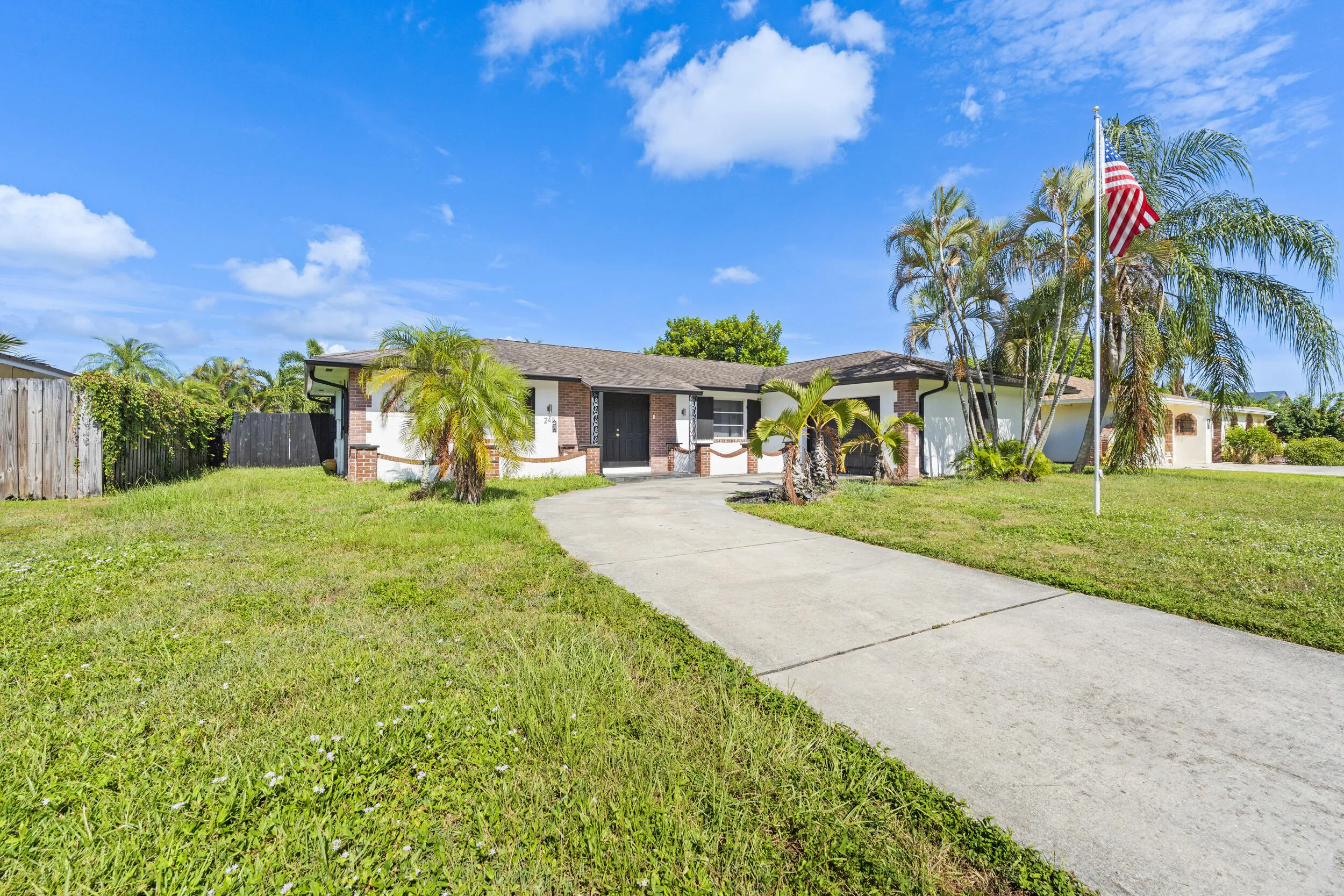 Single-story residence featuring a paved driveway, mature palm trees, and a privacy fence