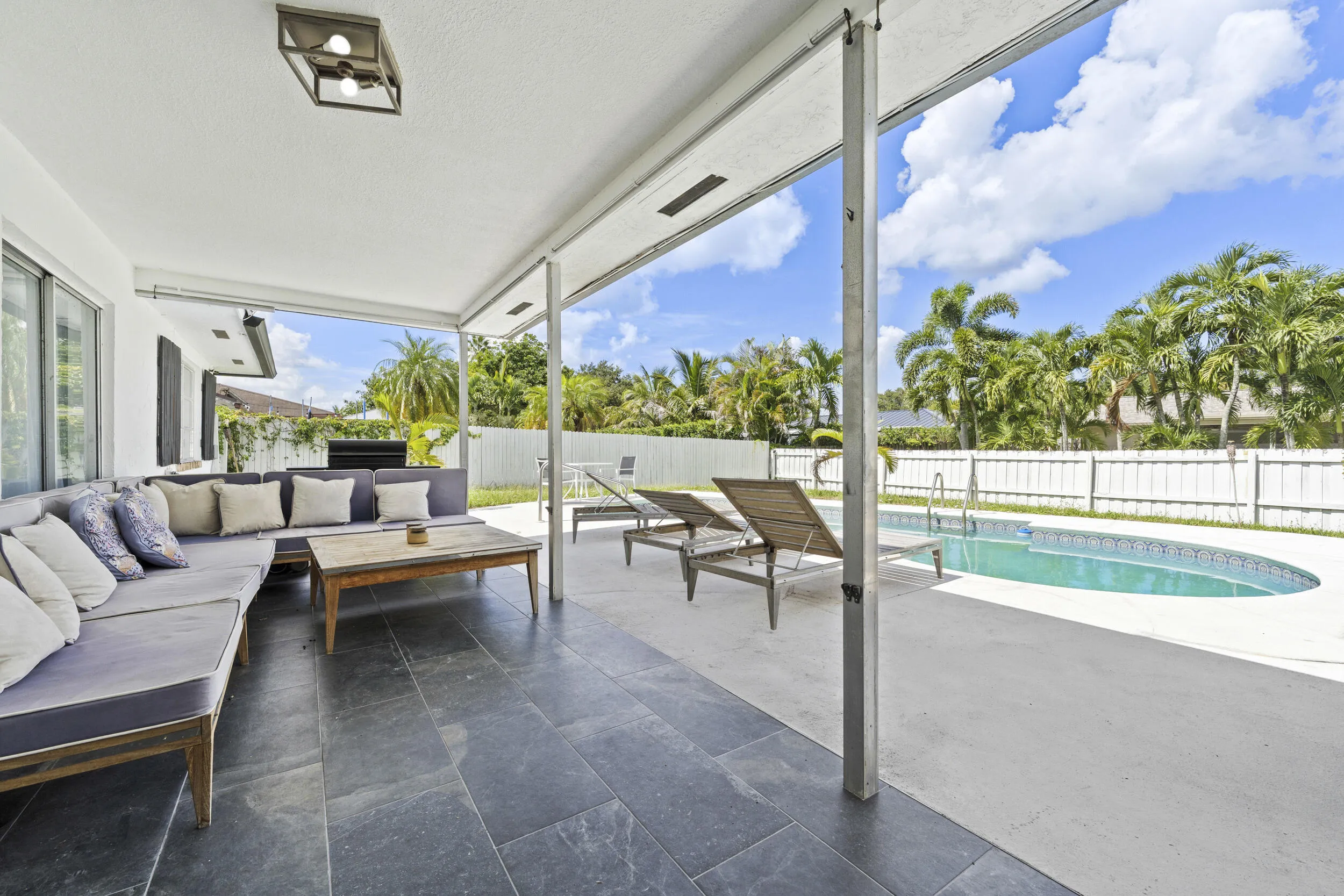 Covered patio with dark tile flooring, expansive concrete decking, and a curved inground swimming pool