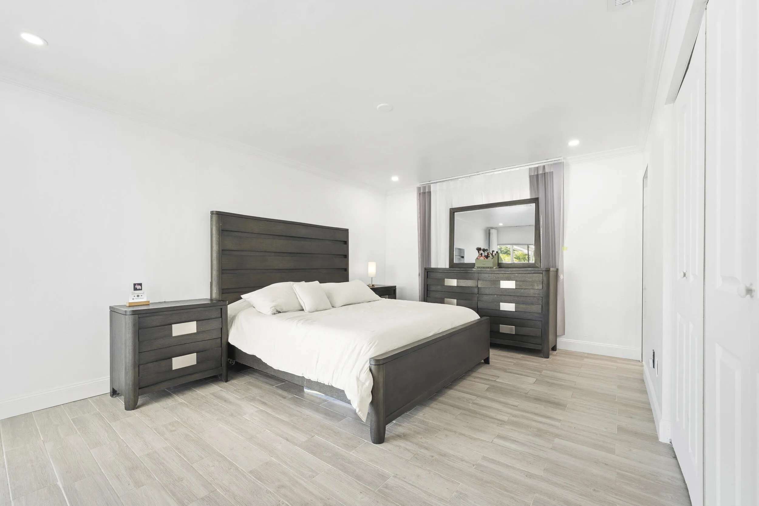 Recessed ceiling lighting illuminates the space, featuring light wood-finish flooring and white bi-fold closet doors
