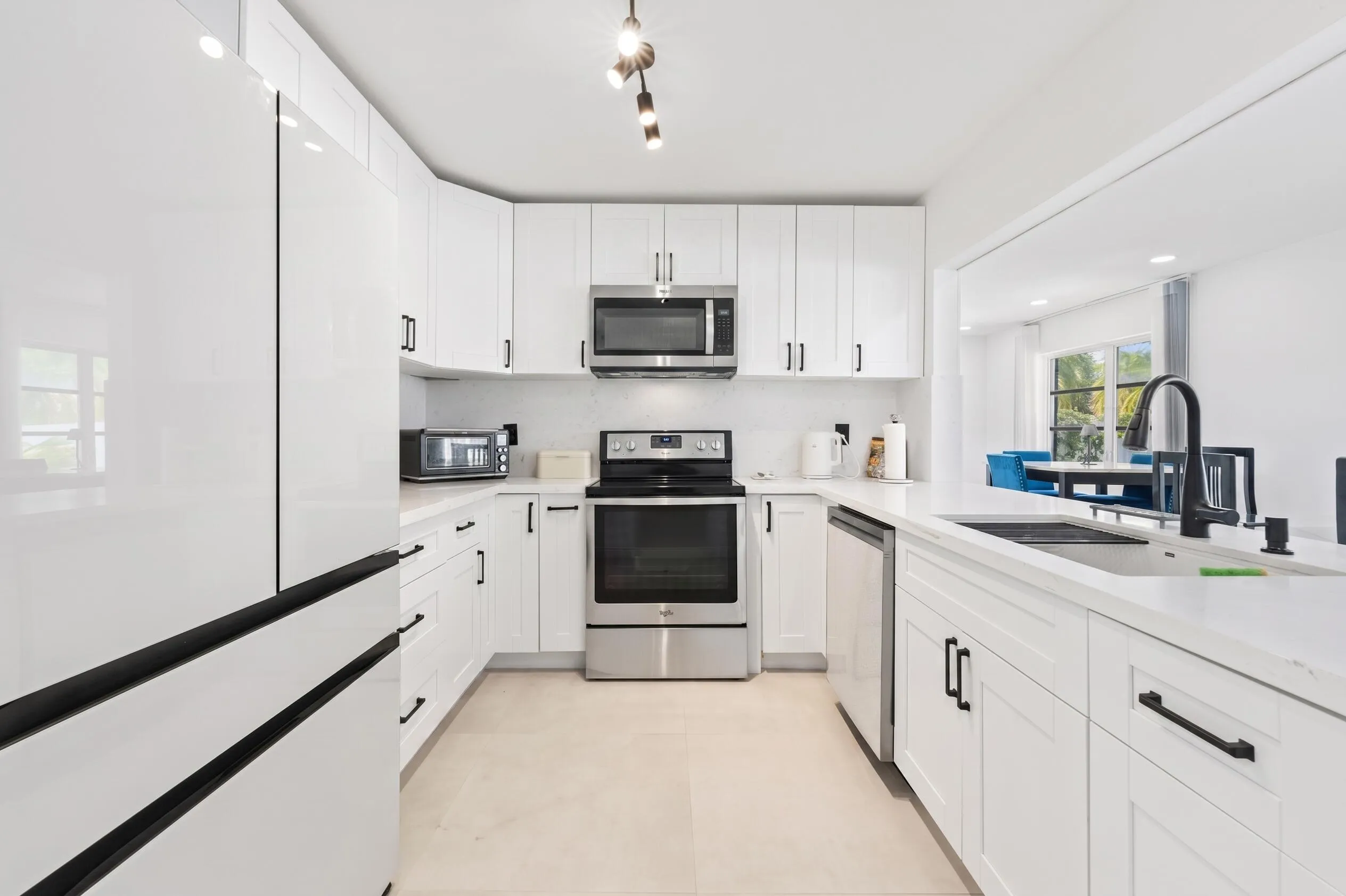 U-shaped kitchen featuring white cabinetry, stainless steel appliances, a stainless steel sink with a black gooseneck faucet, and track lighting