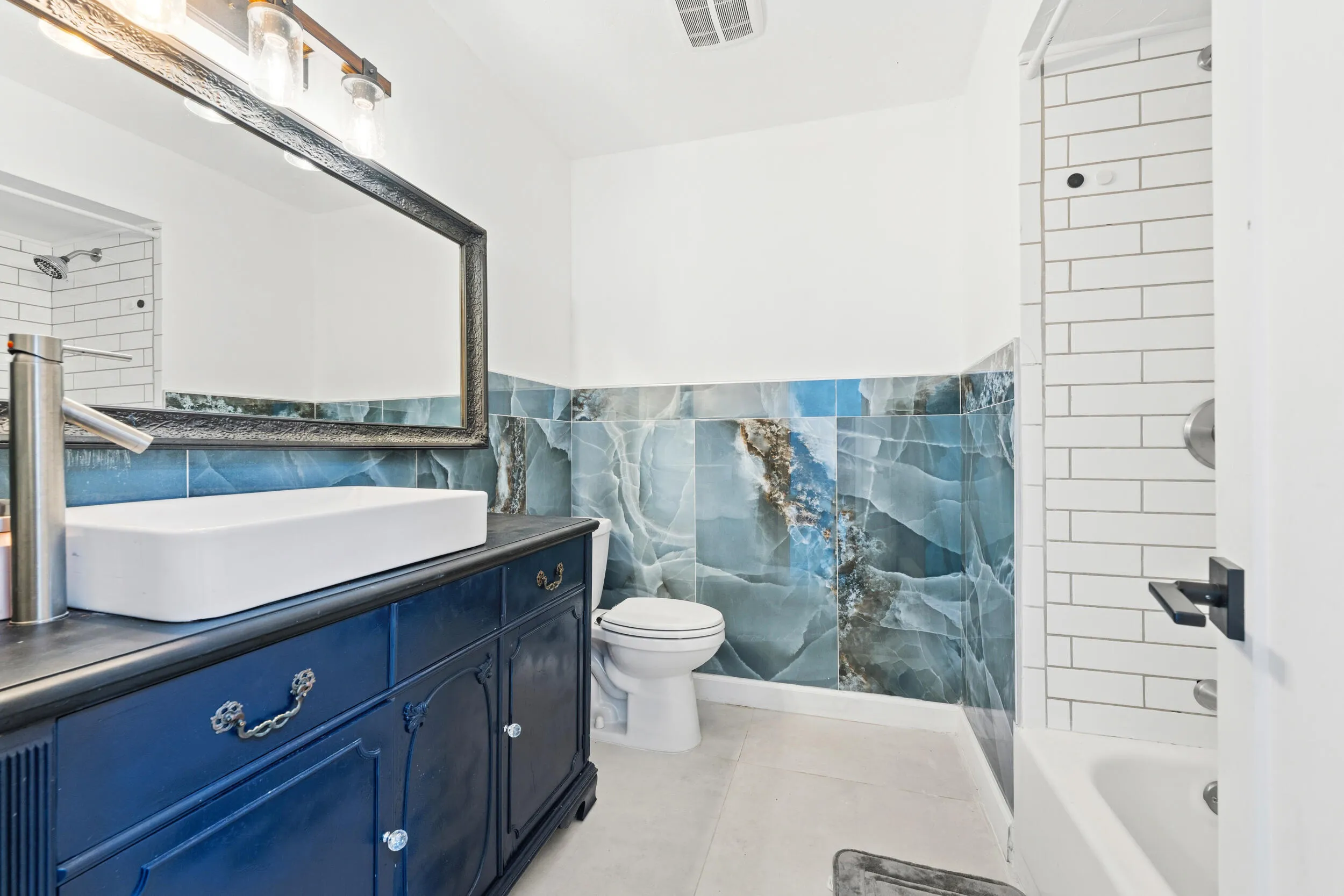Vanity with a rectangular vessel sink and tall faucet, framed mirror, decorative wall tile, and subway-tiled shower
