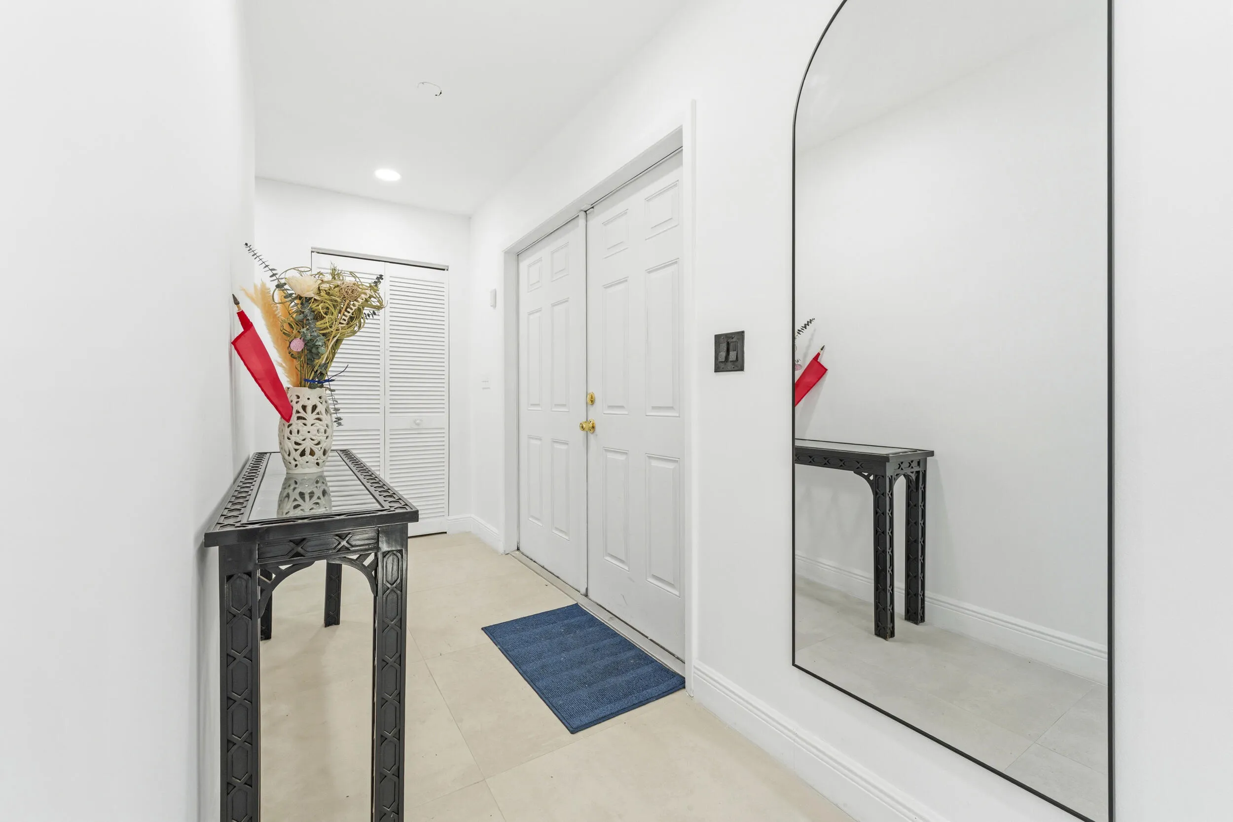 Hallway with light tile flooring, white bi-fold closet doors, and white paneled entry doors