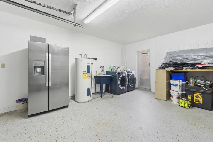 Utility space featuring a water heater, laundry appliances, a utility sink, and a side-by-side refrigerator