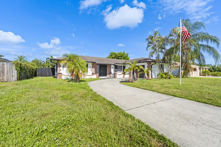 Single-story residence featuring a paved driveway, mature palm trees, and a privacy fence