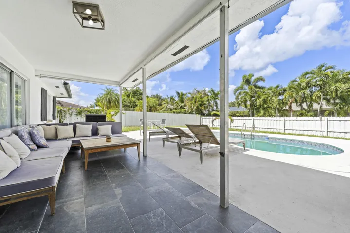 Covered patio with dark tile flooring, expansive concrete decking, and a curved inground swimming pool