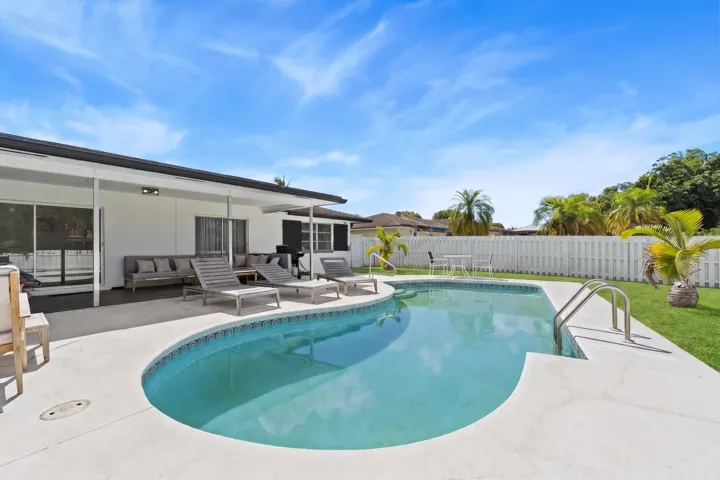 Curved swimming pool with tiled coping and stainless steel handrails, surrounded by a concrete patio