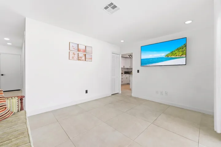 Recessed lighting illuminates the neutral tile flooring and white walls