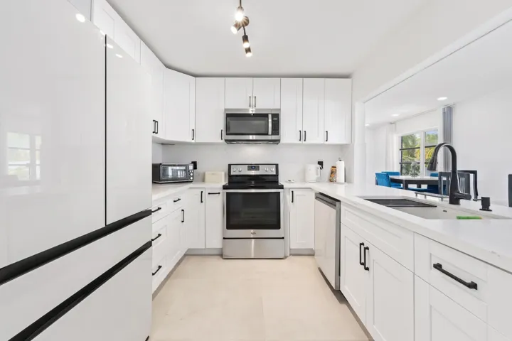 U-shaped kitchen featuring white cabinetry, stainless steel appliances, a stainless steel sink with a black gooseneck faucet, and track lighting