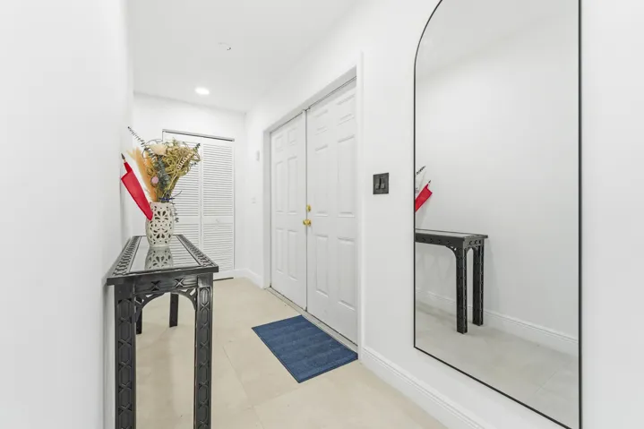 Hallway with light tile flooring, white bi-fold closet doors, and white paneled entry doors