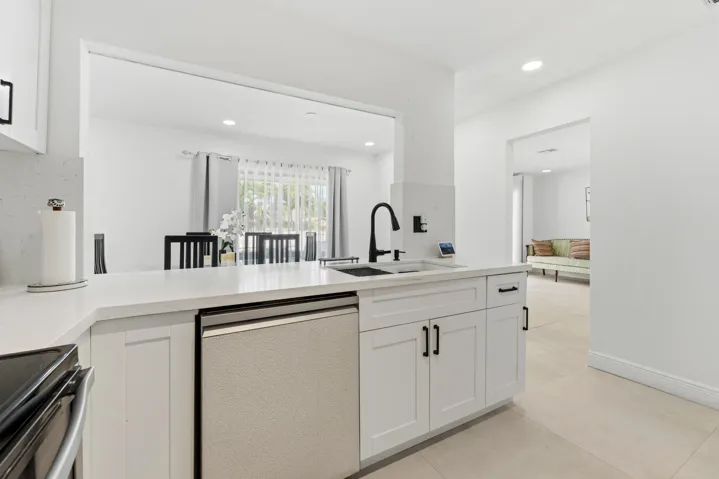 Kitchen featuring white cabinetry, light-toned countertops, a stainless steel dishwasher, and a black gooseneck faucet