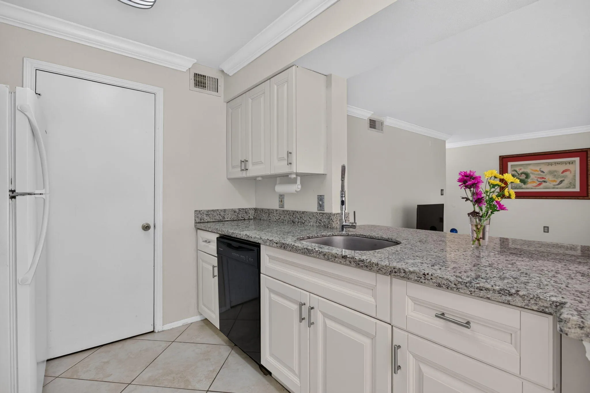 Kitchen featuring white paneled cabinetry, light-toned tiled flooring, a stainless steel sink with a gooseneck faucet, black dishwasher, and speckled countertops