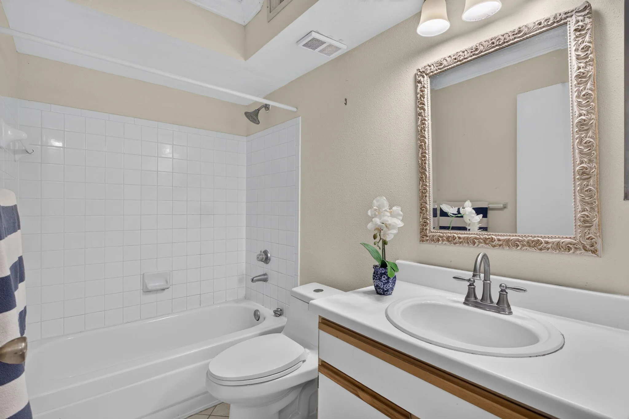 Bathroom featuring a bathtub with subway tile surround, a toilet, a vanity with an integrated sink, and an ornate framed mirror