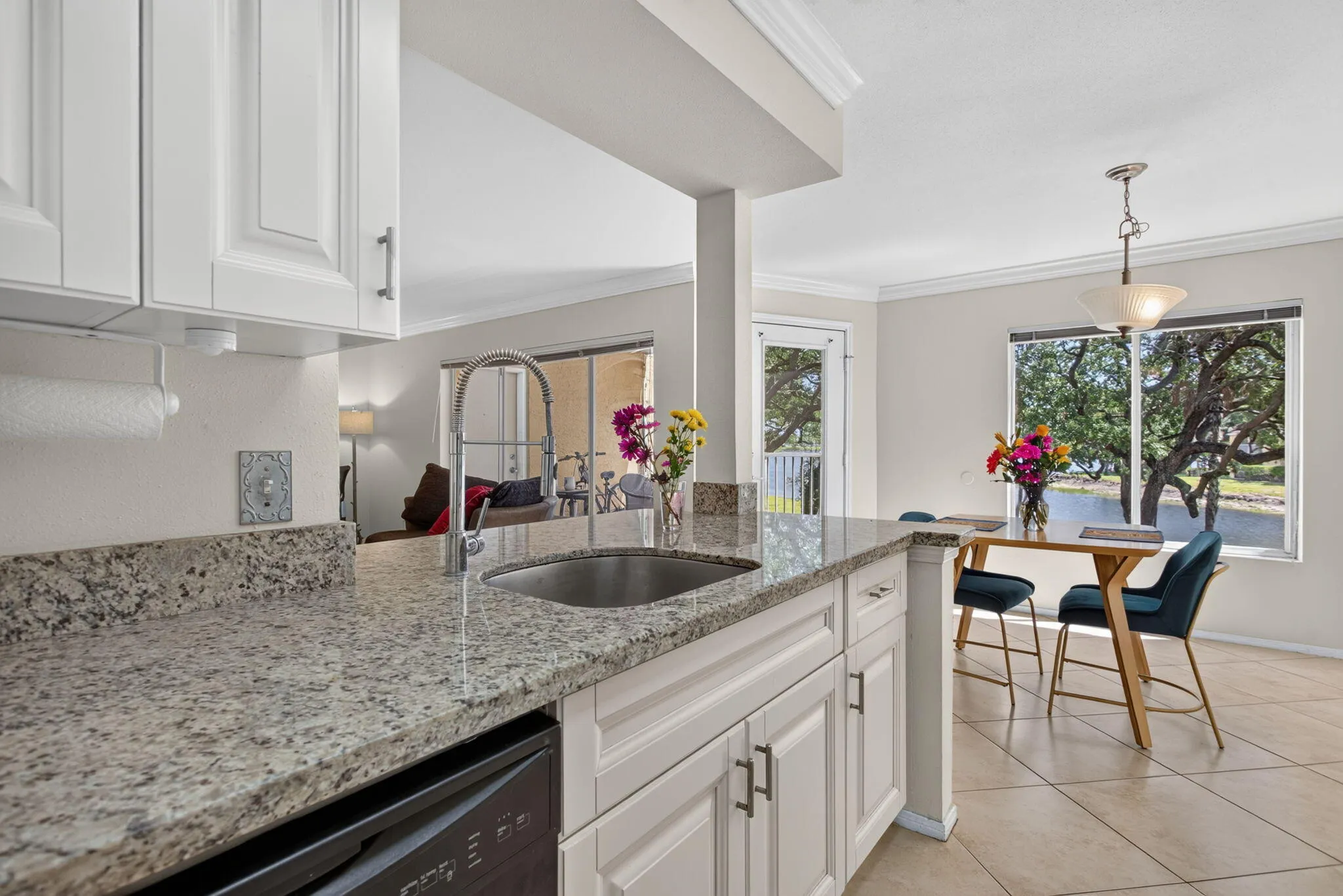 White shaker cabinetry, stone countertops, stainless steel sink, tile flooring, and a rear door with a full-light panel