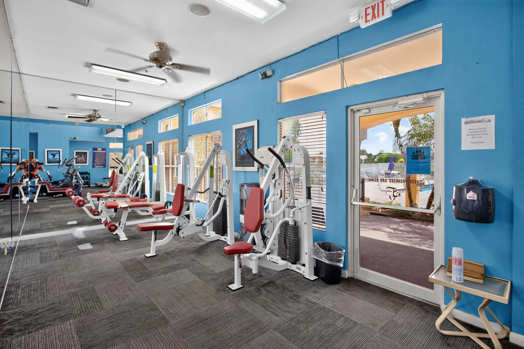 Fitness center with carpet tile flooring, multiple exercise machines, mirrored walls, and a glass-paneled exit door