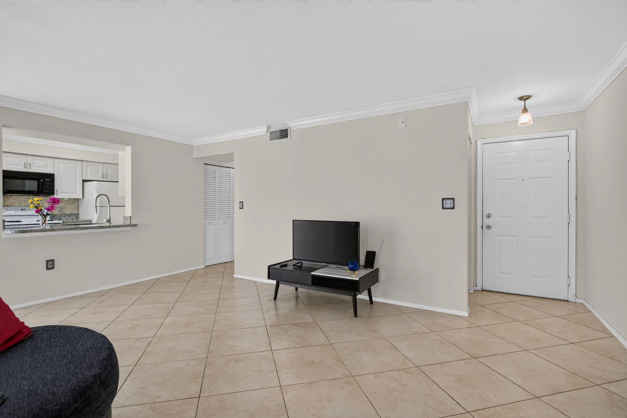 Open-concept layout with tile flooring throughout, crown molding, and a kitchen pass-through featuring stone countertops and white cabinetry