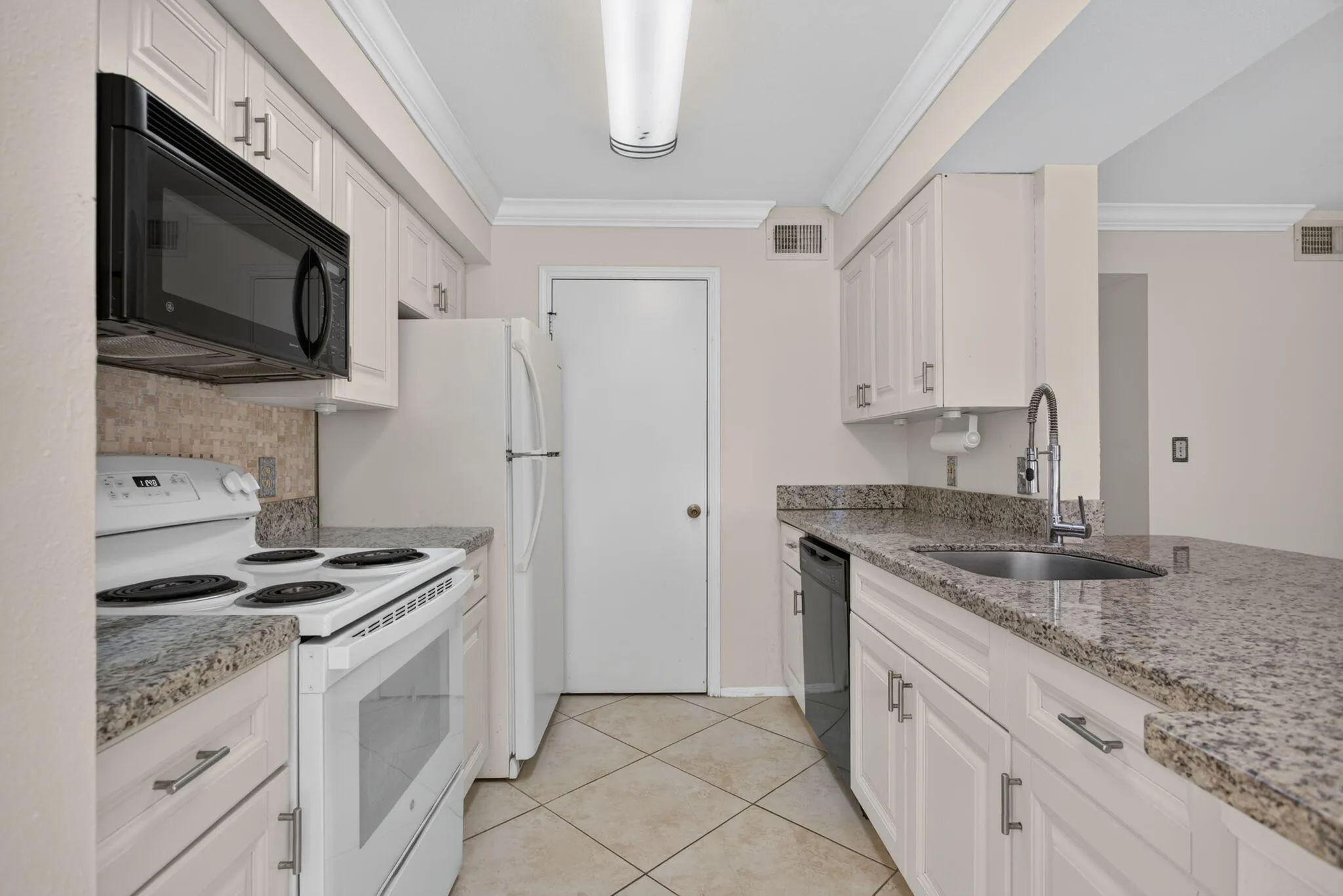 White cabinetry, stone countertops, stainless steel sink, tiled flooring, and crown molding