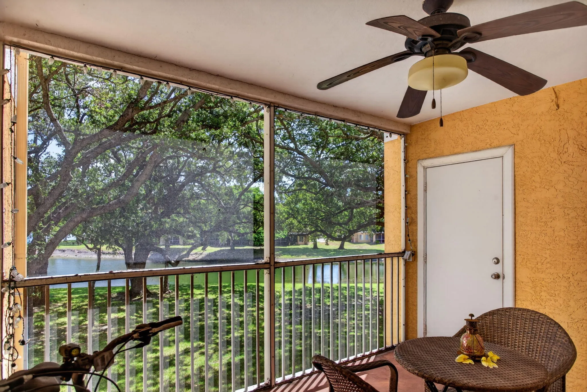 Screened balcony with textured exterior wall, ceiling fan with integrated lighting, and a white access door