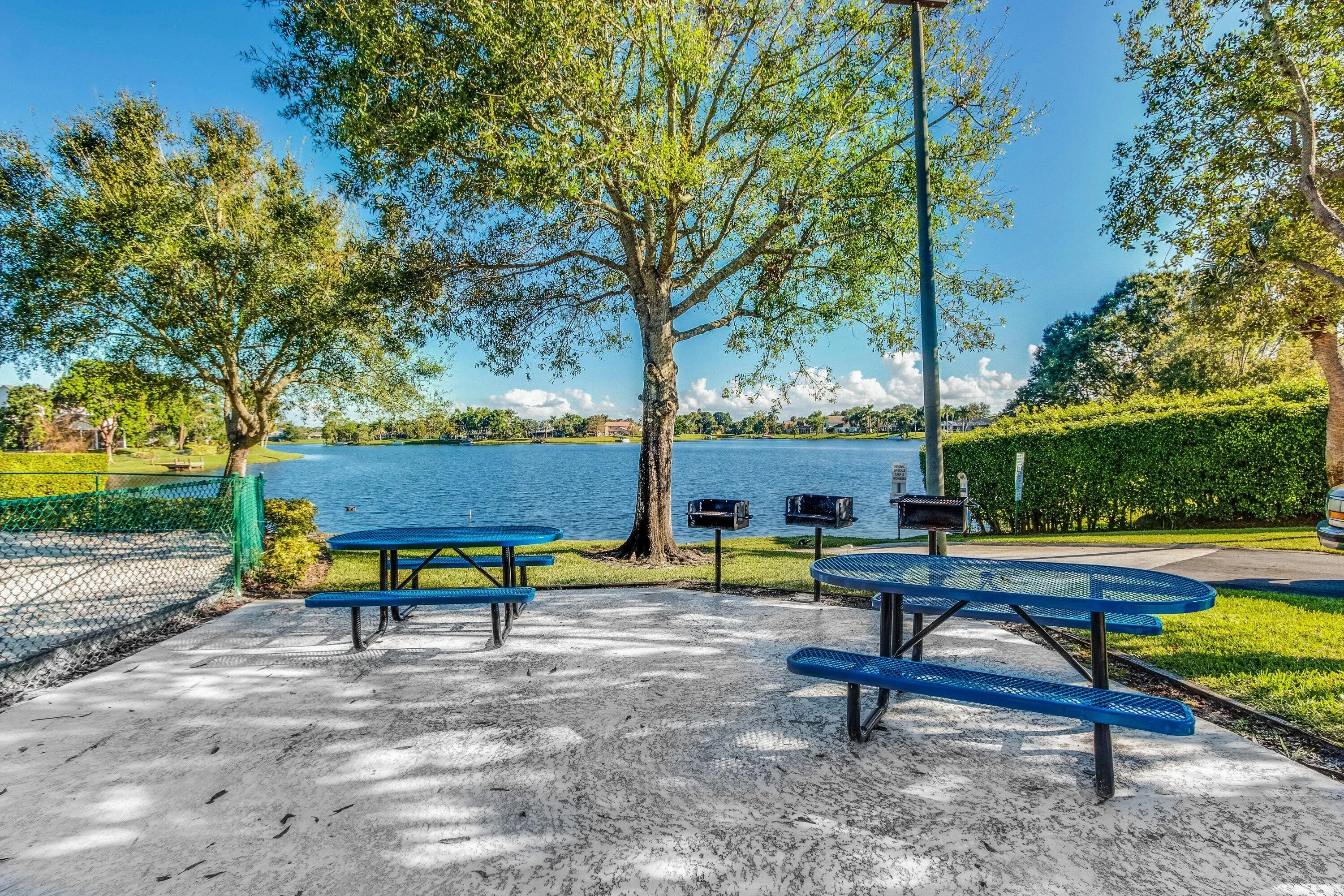 Lakeside patio area with two picnic tables and two permanent grills, surrounded by mature trees